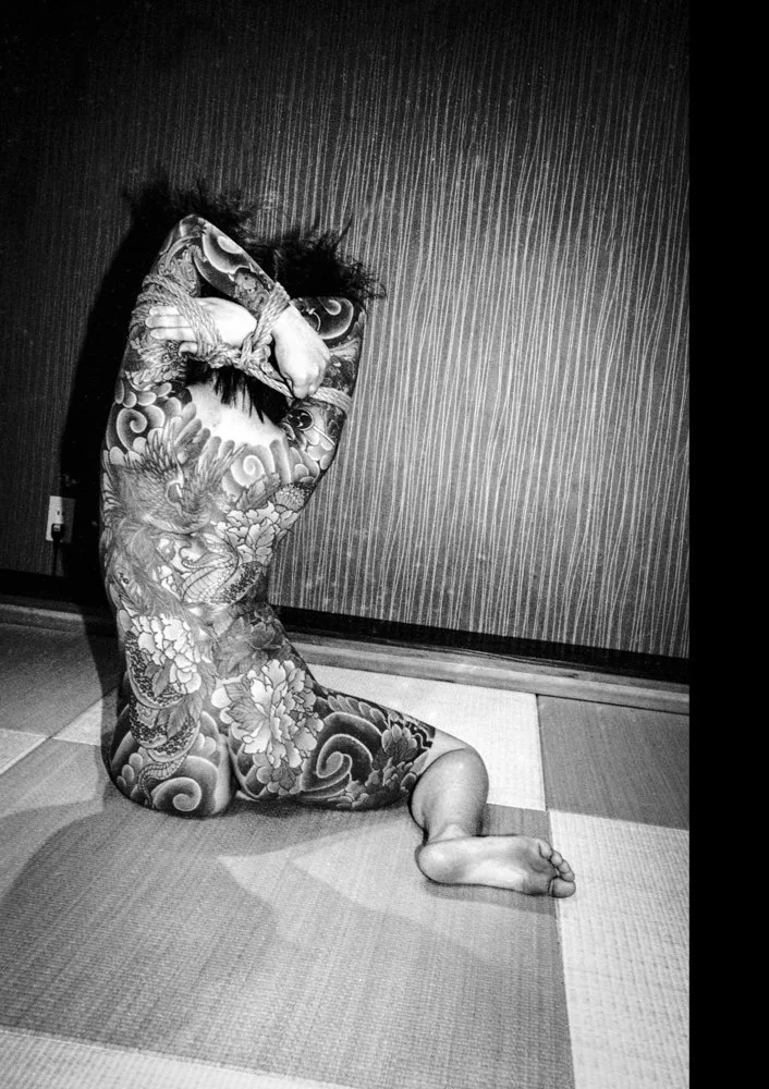 Black and white portrait of a seated and heavily tattooed Yakuza member from the back.