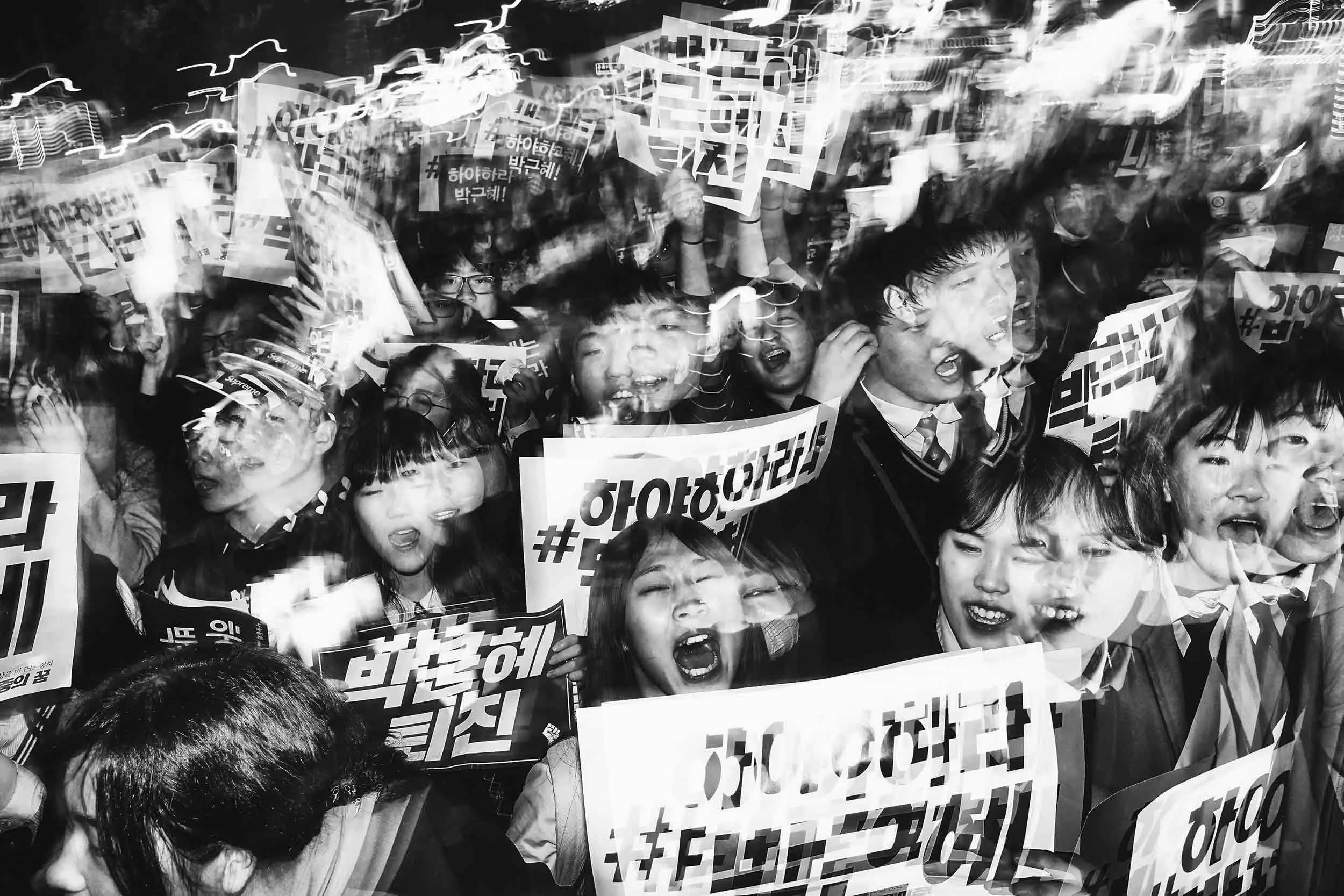 Black and white photo of South Korean student protesters hold signs at an anti-president demonstration.