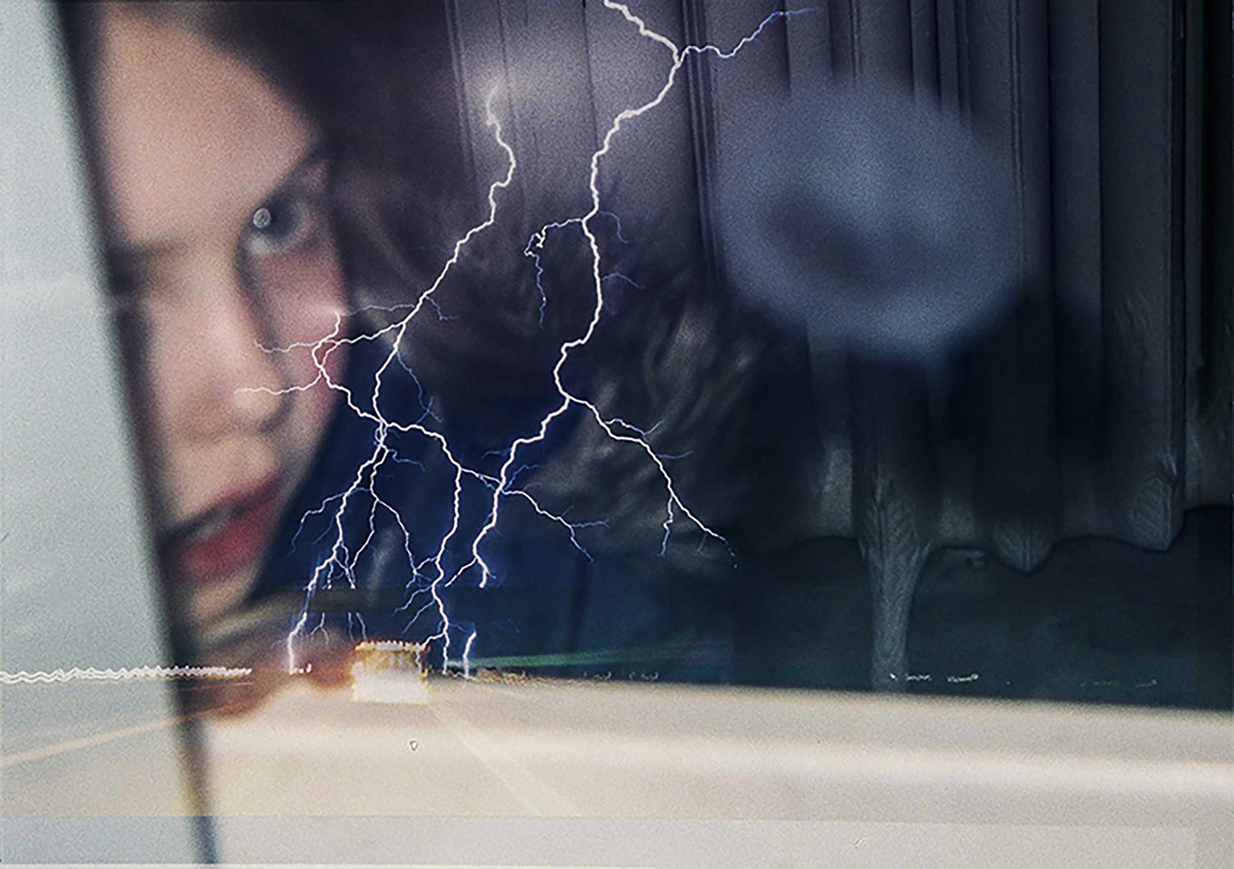A young girl looks through a window that has lighting reflected in it.