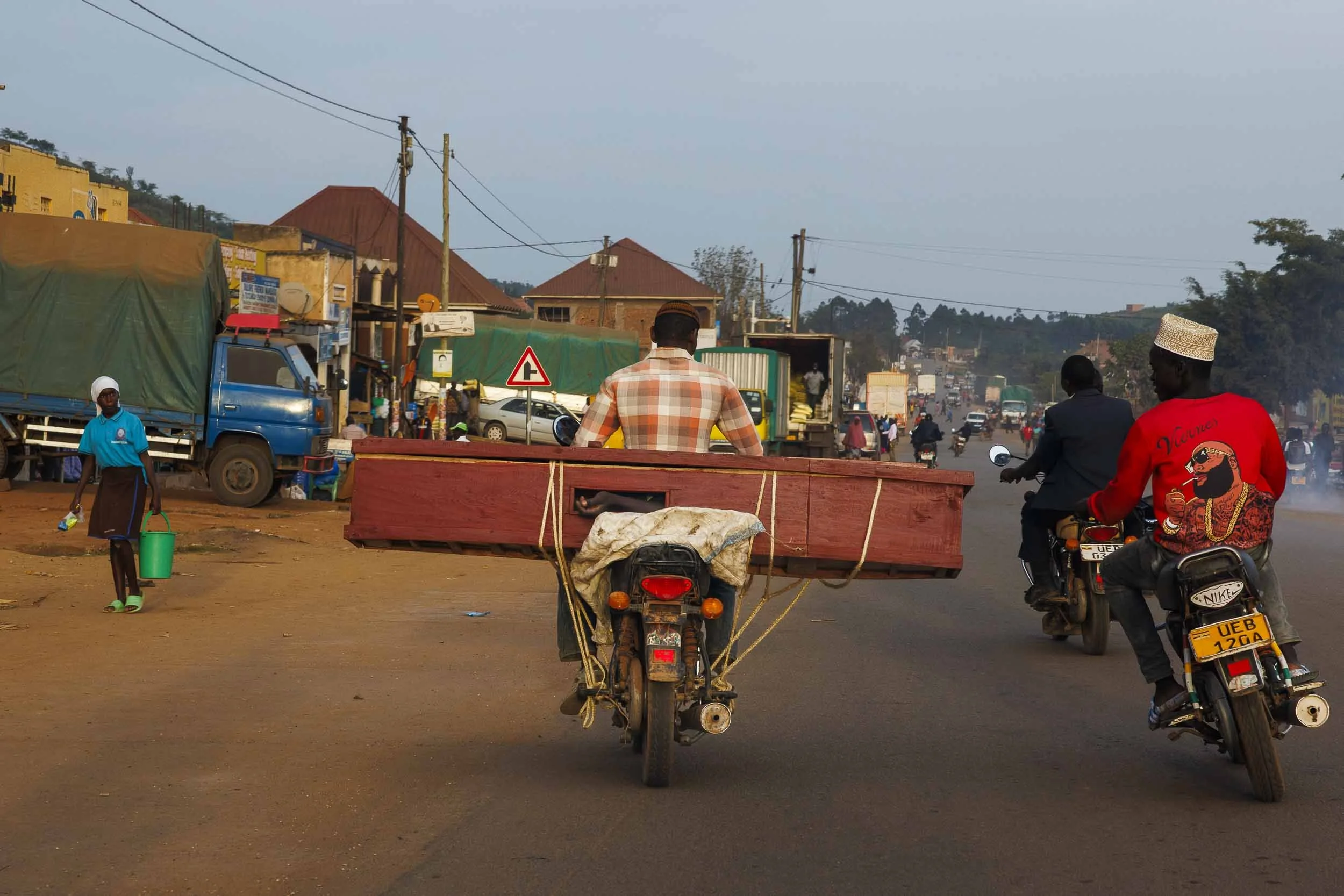 A boda bod driver drives on the road in Uganda carrying a coffin on the back of his motorbike.