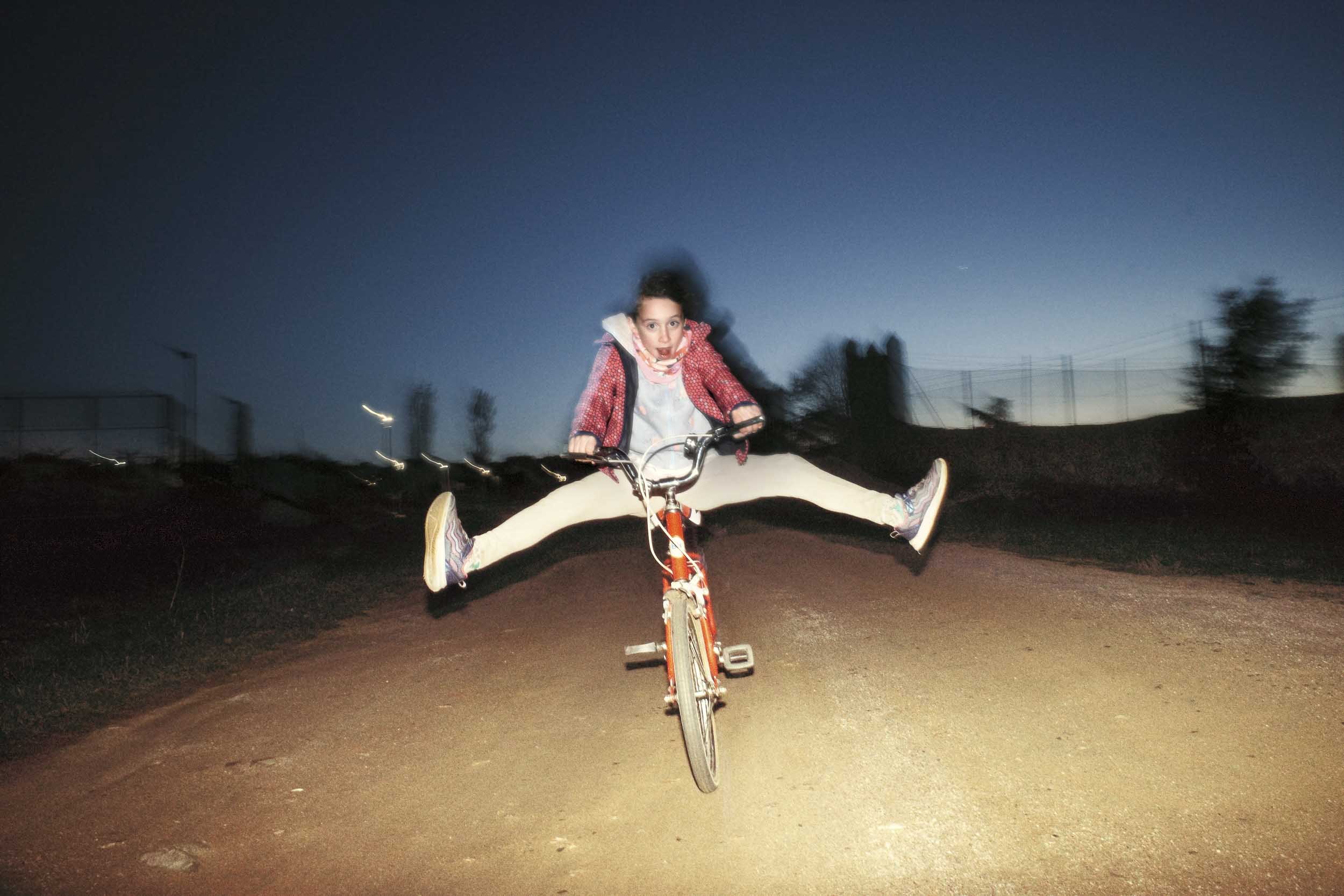 A young boy rides a bike towards the camera and spreads his legs wide.