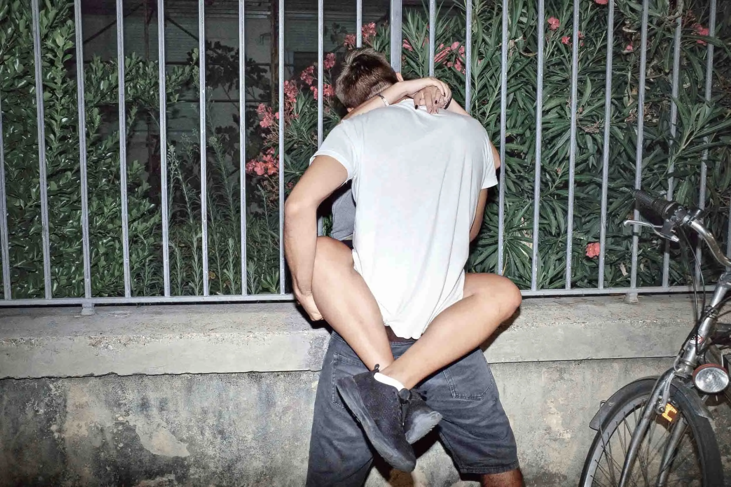 A man lifts a lady up on a ledge as she wraps her arms around him and they kiss passionately.