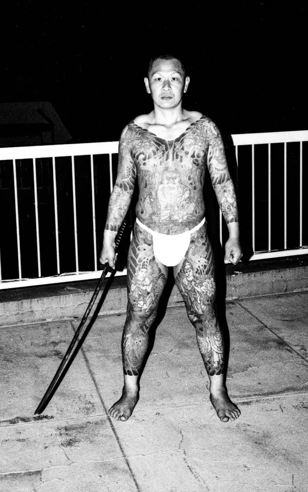 Black and white portrait of a heavily tattooed Yakuza member holding a sword.