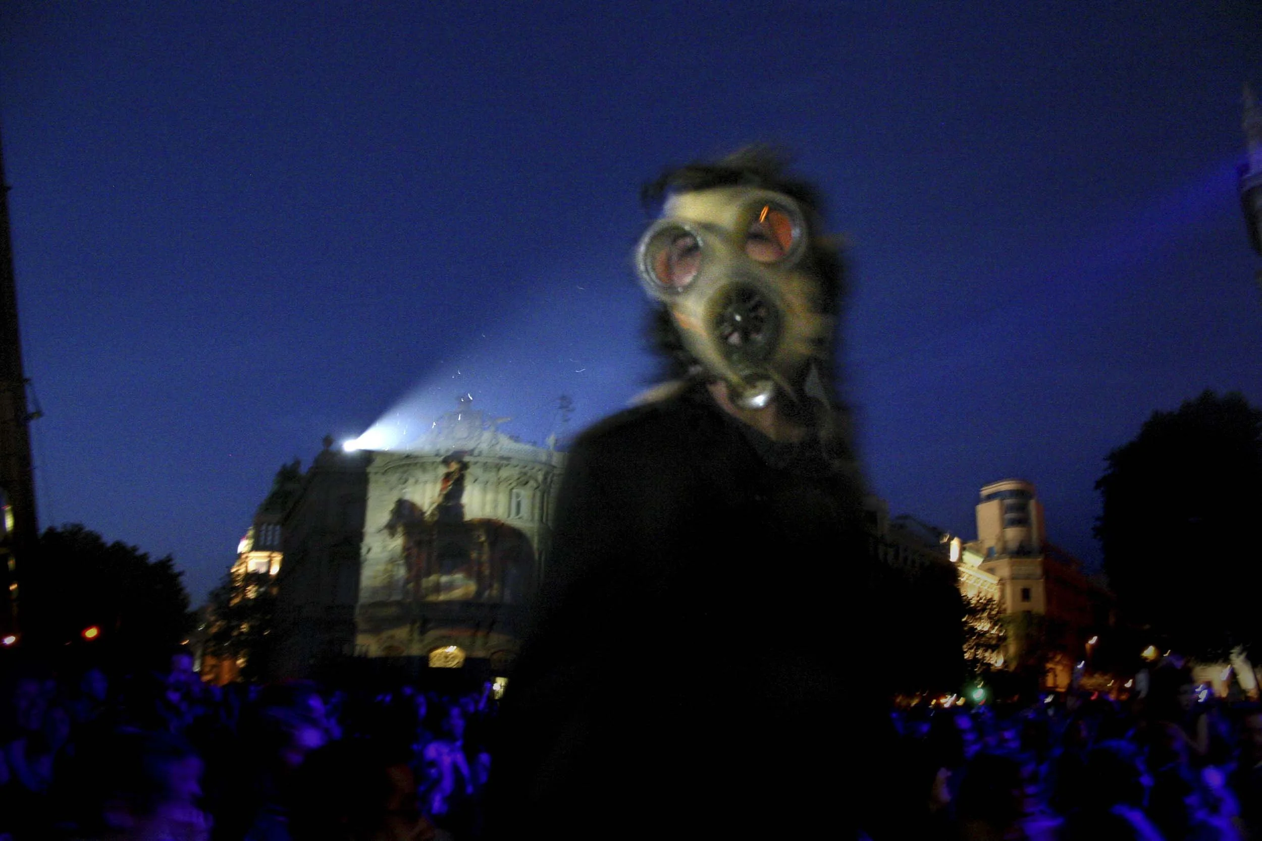 Person in a gas mask standing in front of a statue and a blue sky in the evening.