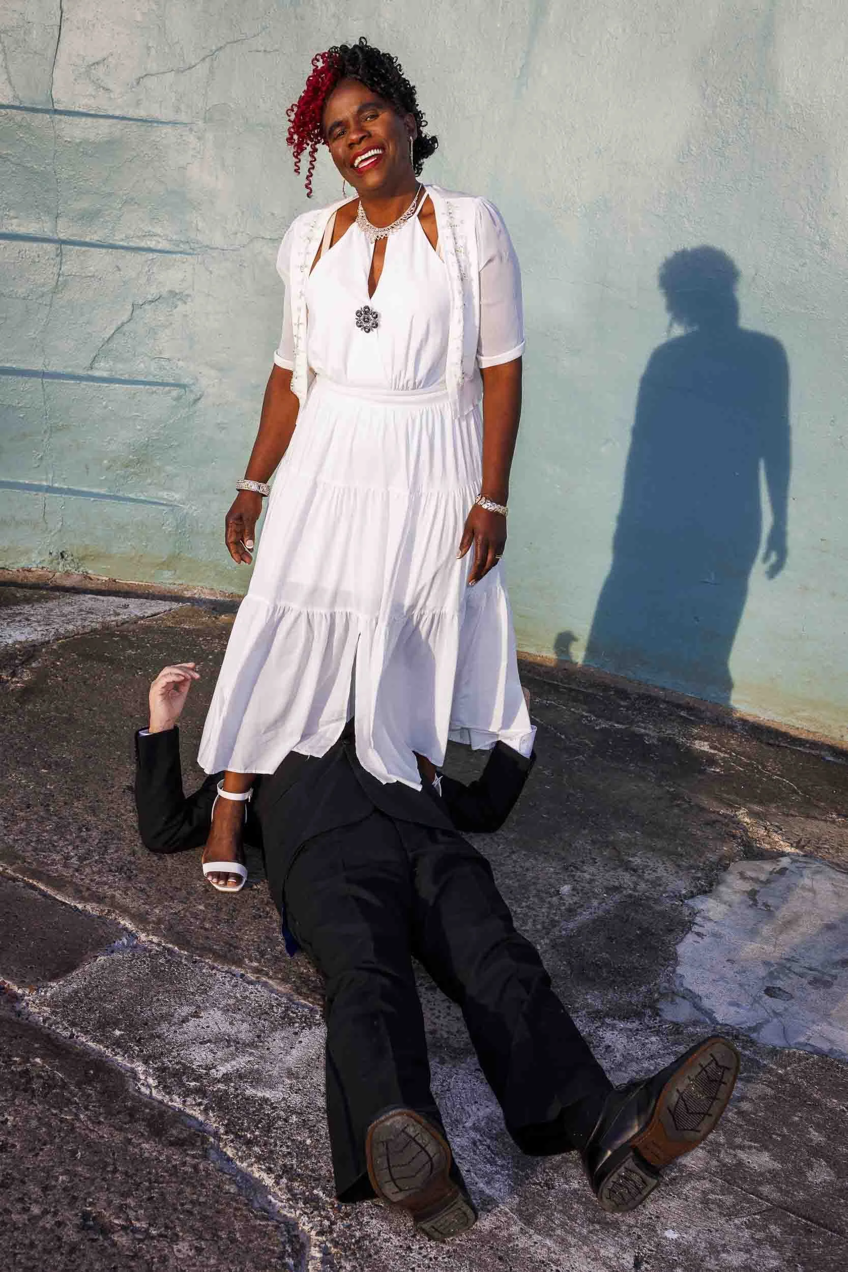 African wife standing over her white husband who lays on the floor in their humorous wedding photos.
