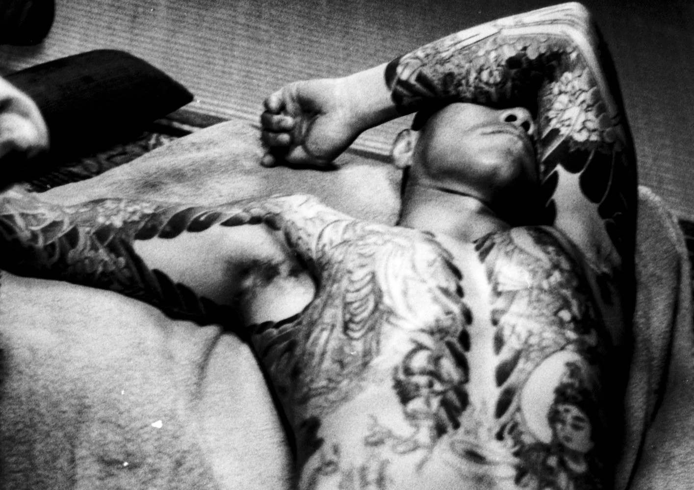Black and white portrait of a heavily tattooed Yakuza member who is lying on the ground and partly obscuring his face with his arm.