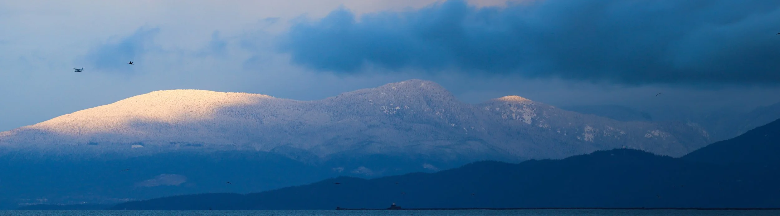 Scenic view of snow-covered mountains with a cloudy sky and a body of water in the foreground.