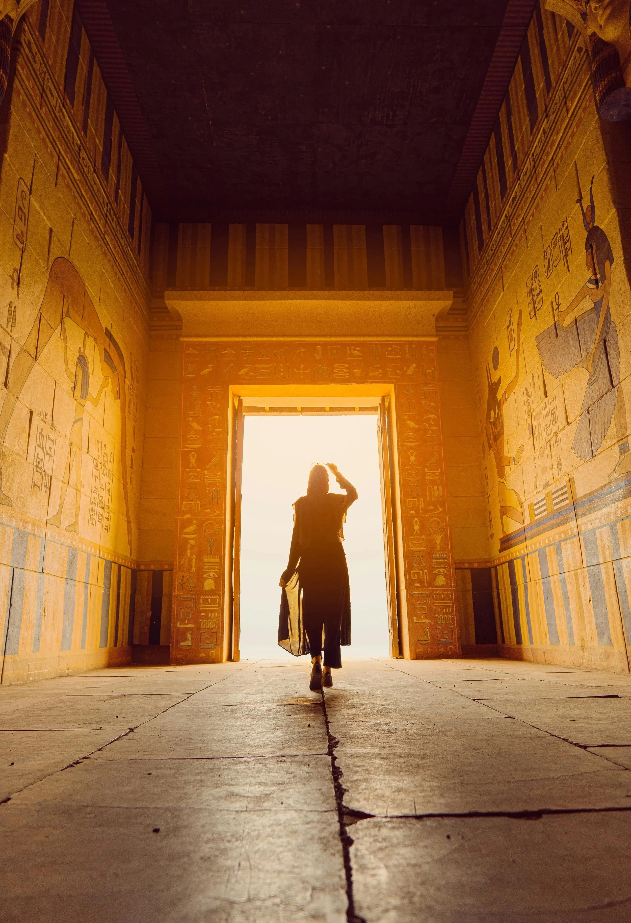 A person walking through an Egyptian temple with hieroglyphic walls at sunset, backlit by the bright open doorway.