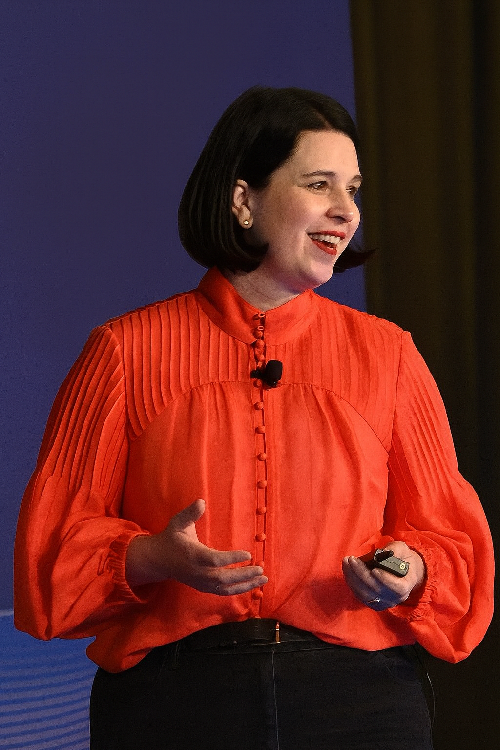 Karlee speaking at a conference in a bright orange shirt with a purple background