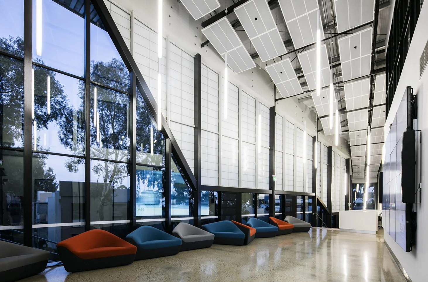 Modern interior lobby with large glass windows, colorful lounge chairs, and ceiling panels with lighting fixtures.