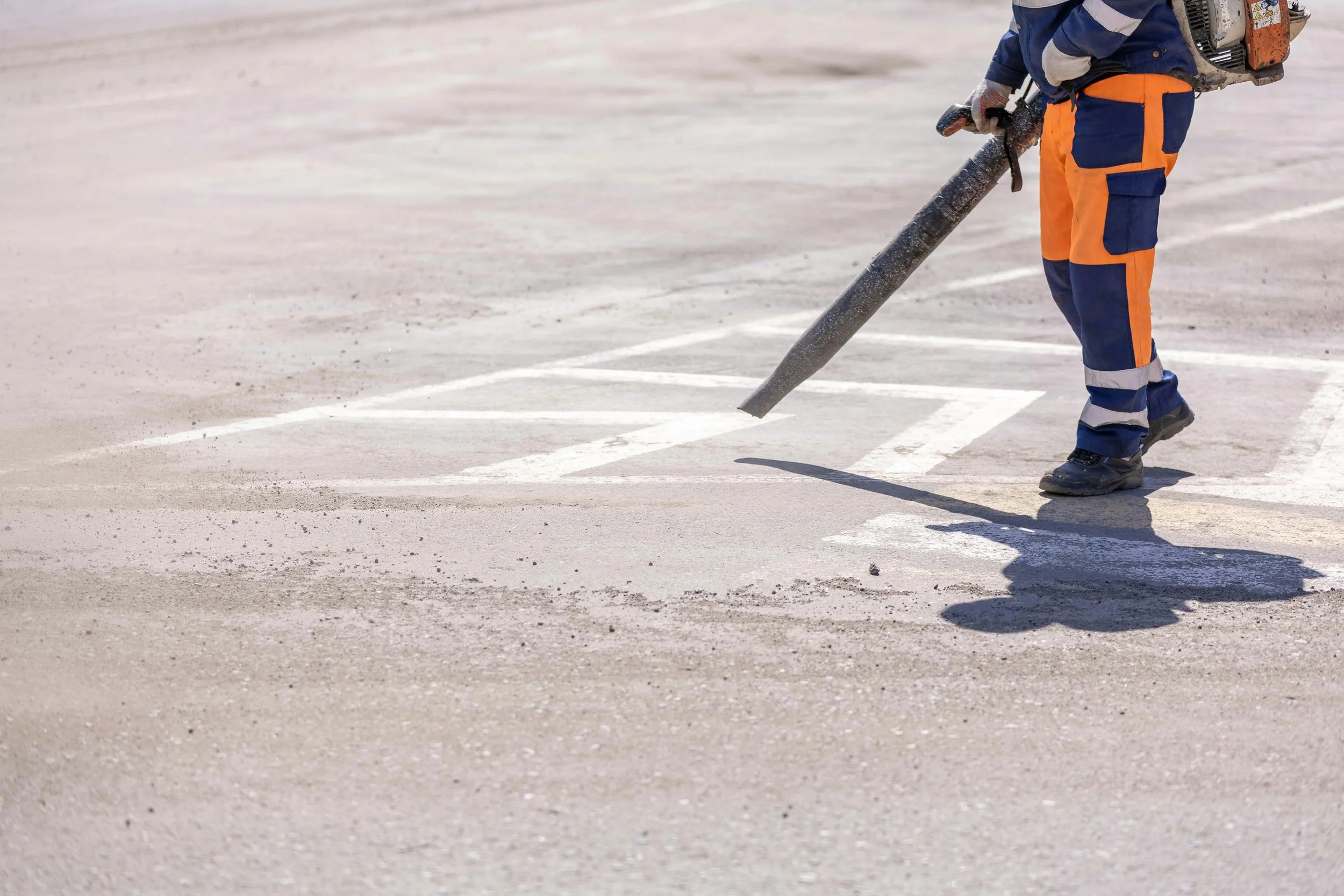 Worker in safety uniform using a power tool to paint parking lot lines.
