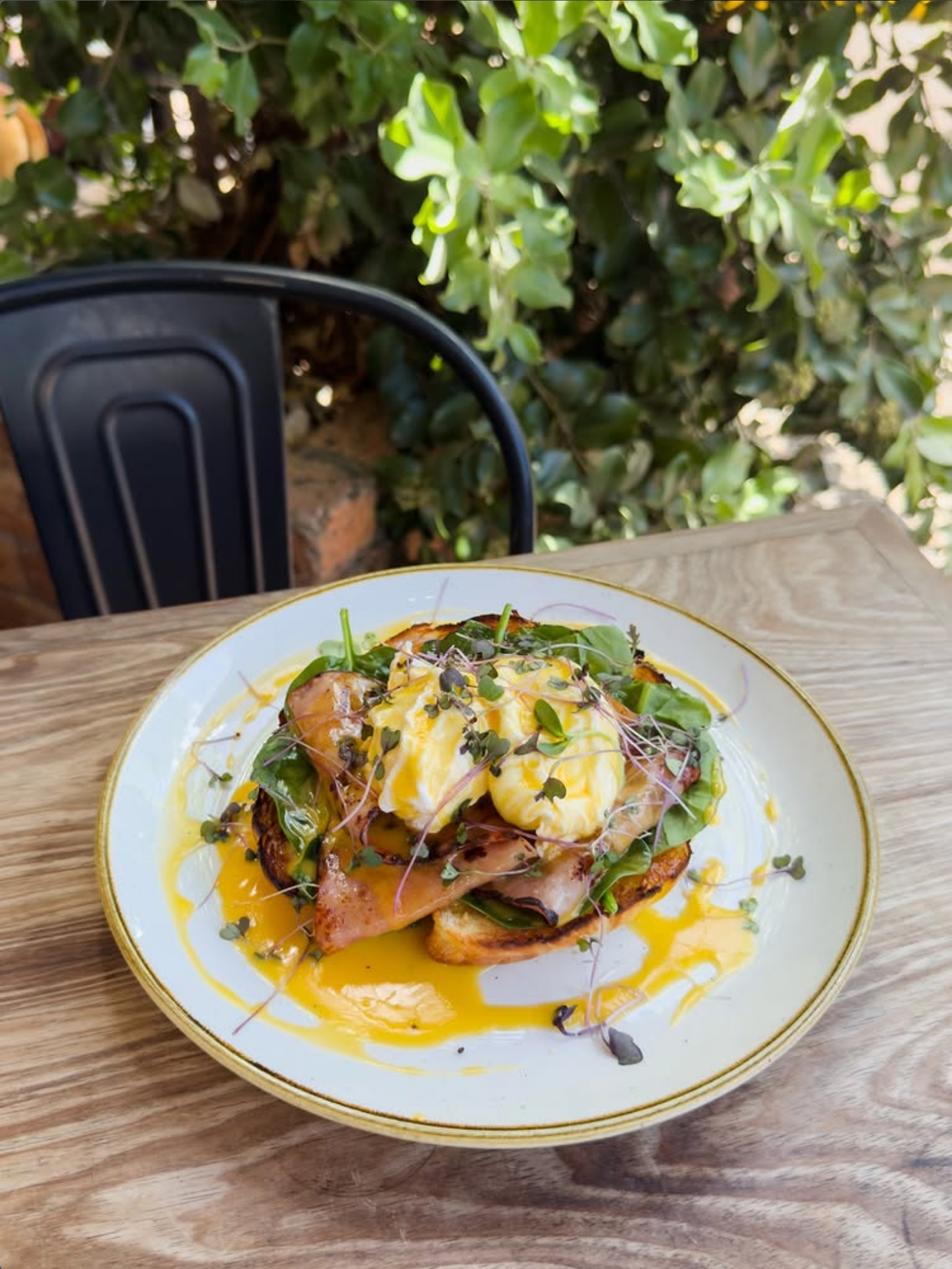 A plate of food with poached eggs, greens, and sauce on a wooden table outdoors