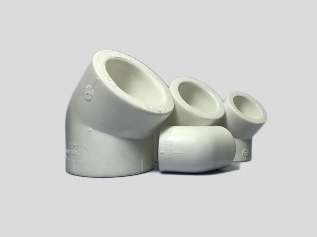 Four white PVC pipe fittings of different sizes arranged on a gray background.