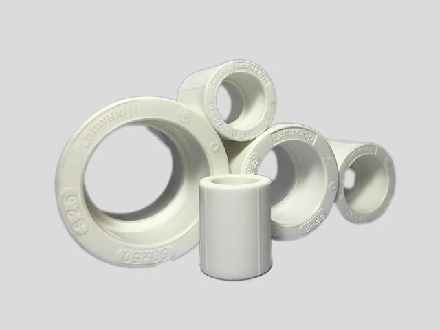 A collection of white plastic pipe fittings with various diameters arranged on a plain background.