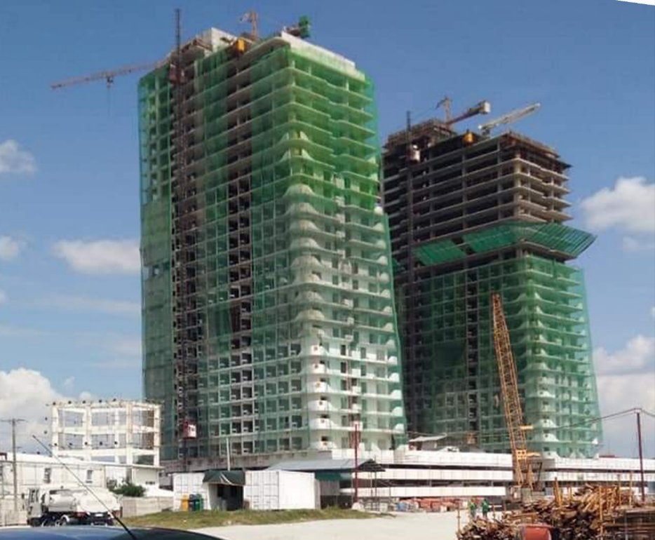 Under construction high-rise buildings covered with green safety netting at a construction site with cranes.