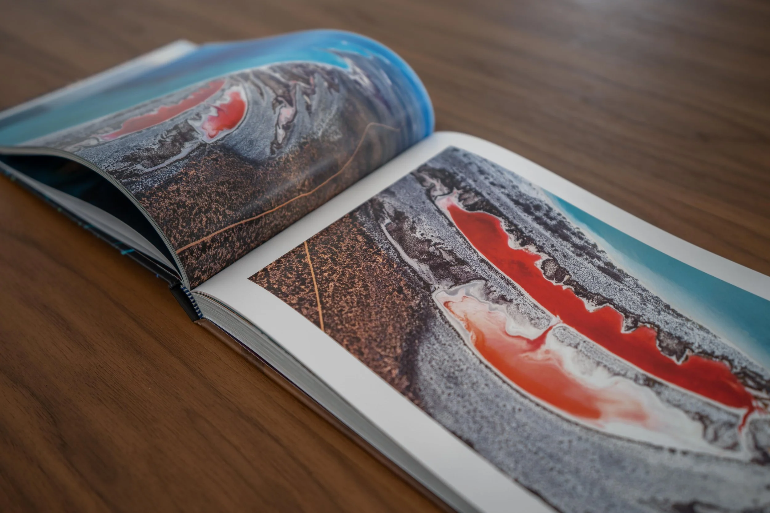 Open magazine on a wooden surface displaying colorful abstract artwork with shades of red, black, white, and blue.