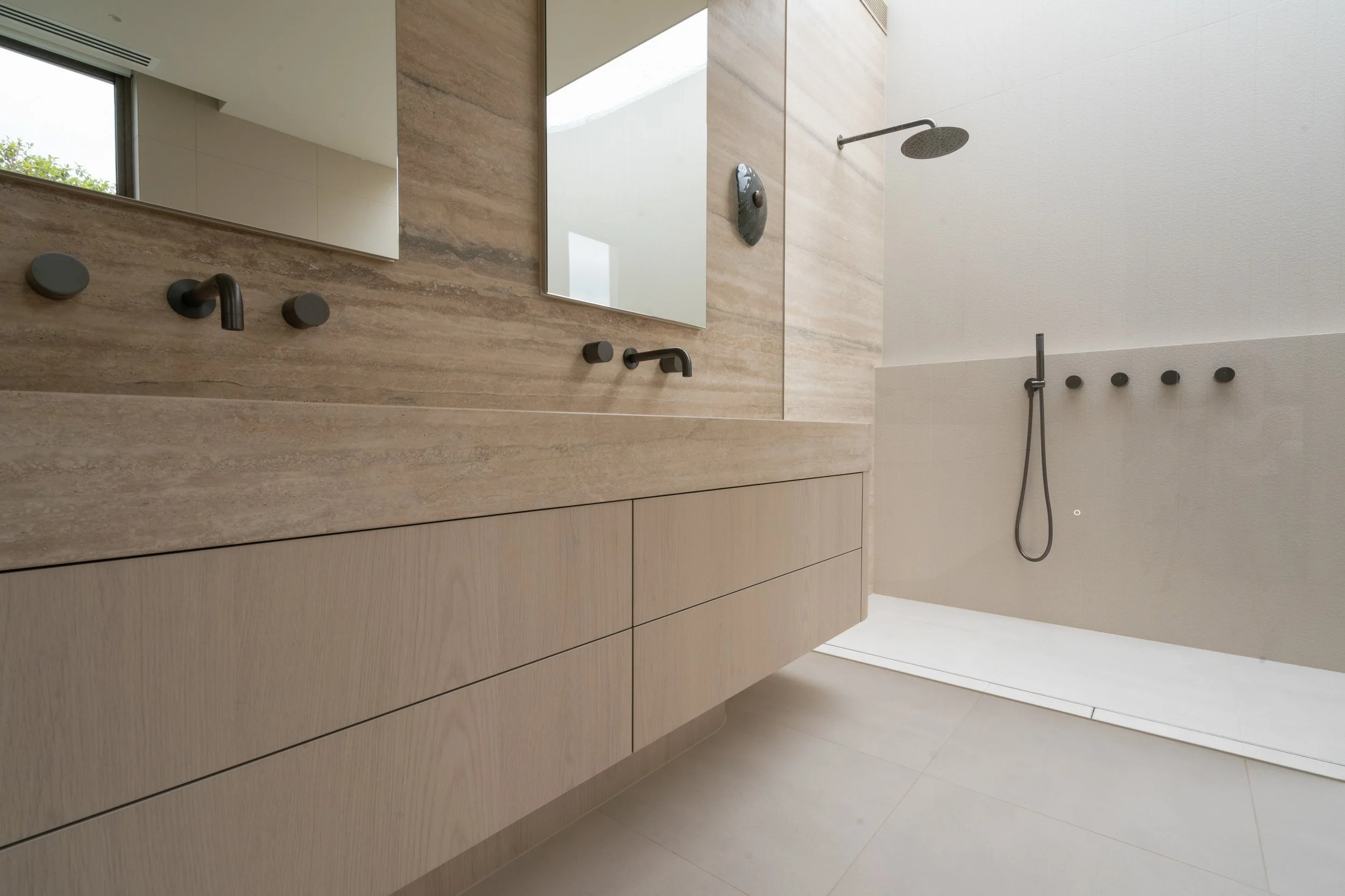 Travertine vanity with backlit mirror and gunmetal tapware, Melbourne bathroom