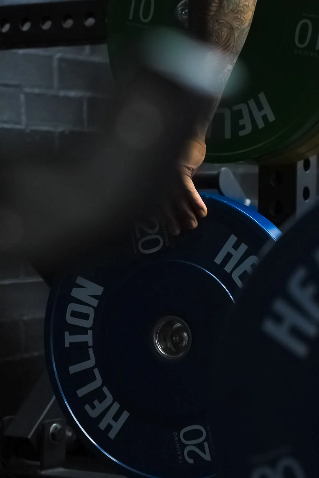Close-up of a hand holding a weight plate with the text "HEALT" visible, rest of the plate obscured and a green container in the background.