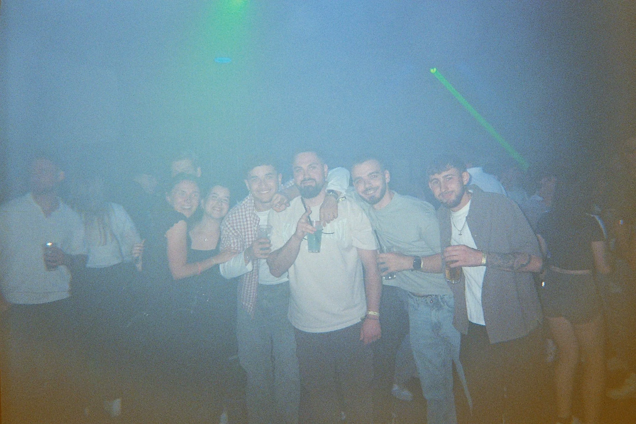 Eine Gruppe junger Menschen, die in einem dunklen Raum mit Disco-Licht feiern, mit einigen Getränken in den Händen, lachen und Freude zeigen.