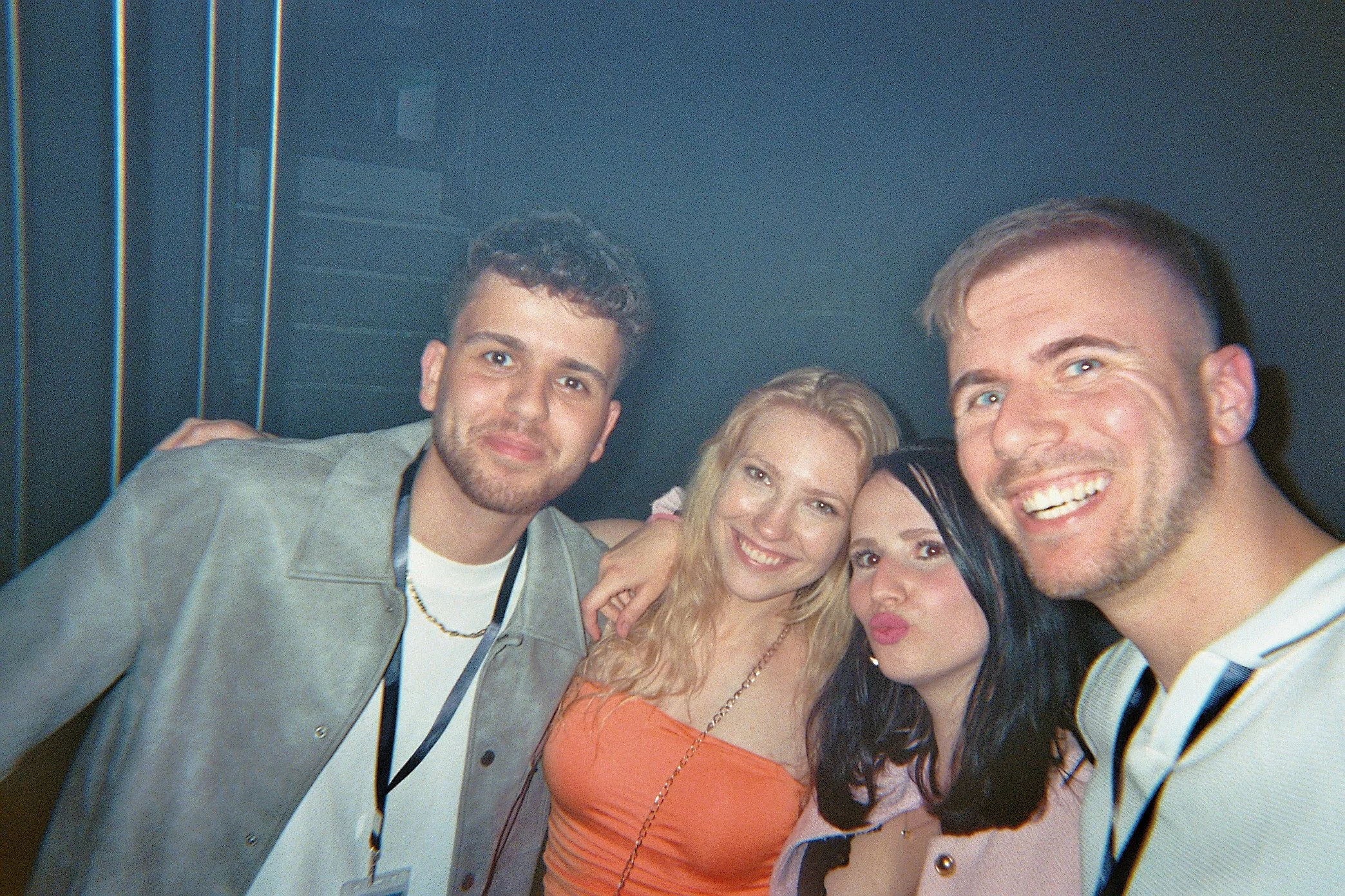 Vier junge Leute beim Feiern in einer dunklen Umgebung, lachen und posieren für das Gruppenfoto.