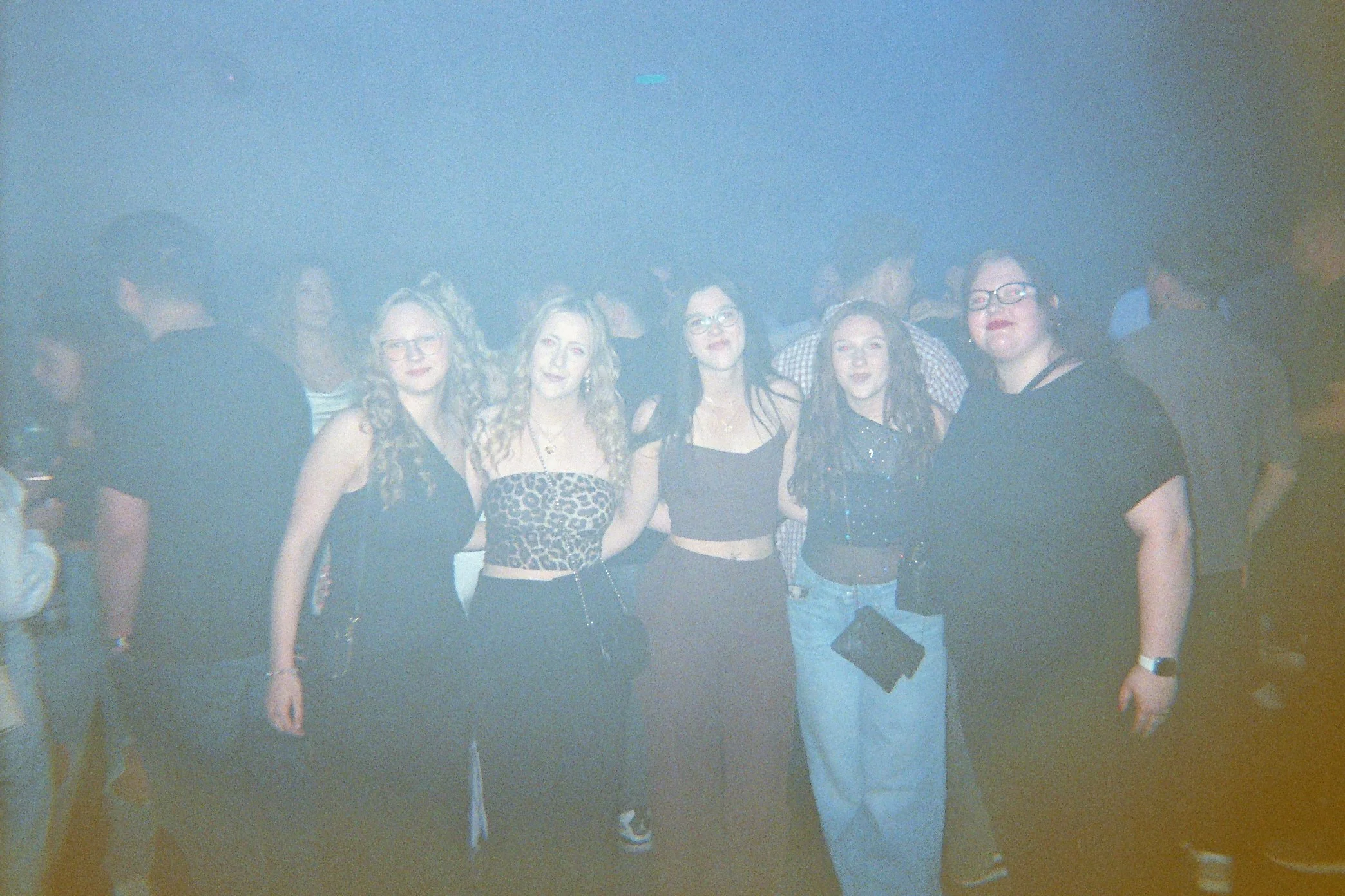 Fünf junge Frauen in einem dunklen Raum, vermutlich eine Party oder ein Club, stehen nebeneinander und posieren für das Foto.