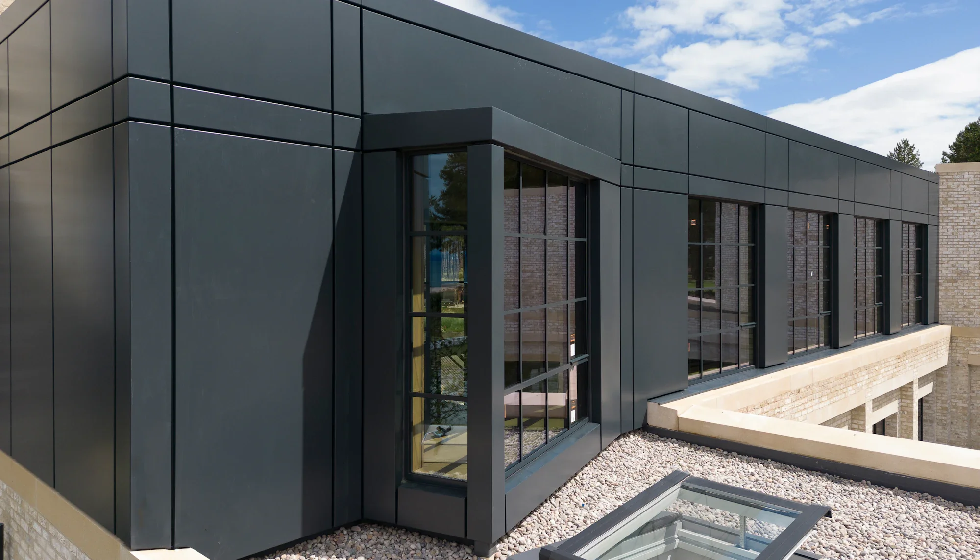 Industrial building with black metal cladding, large glass windows, and a gravel rooftop