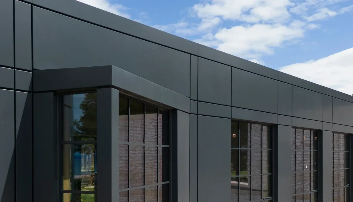 Modern building with dark gray exterior panels and large glass windows, under a partly cloudy sky.
