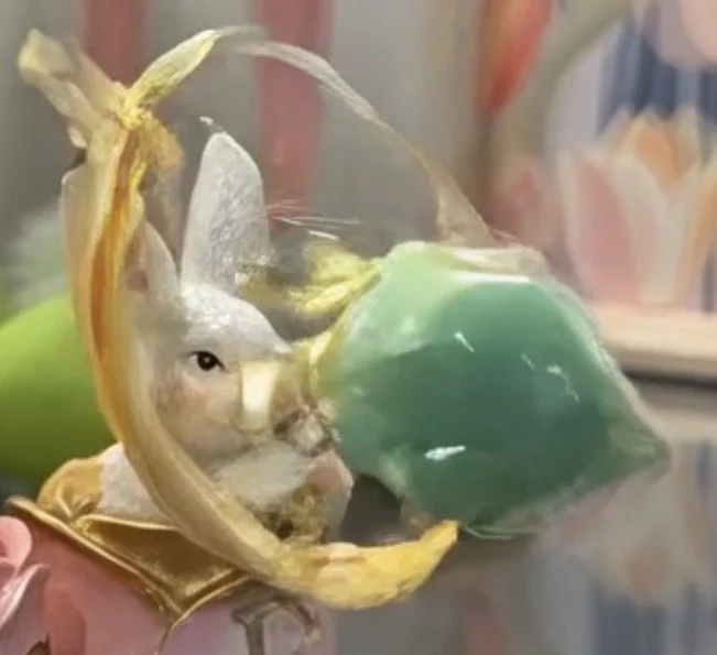 A close-up of a bunny’s face peeking through a plastic bag with colorful items inside.