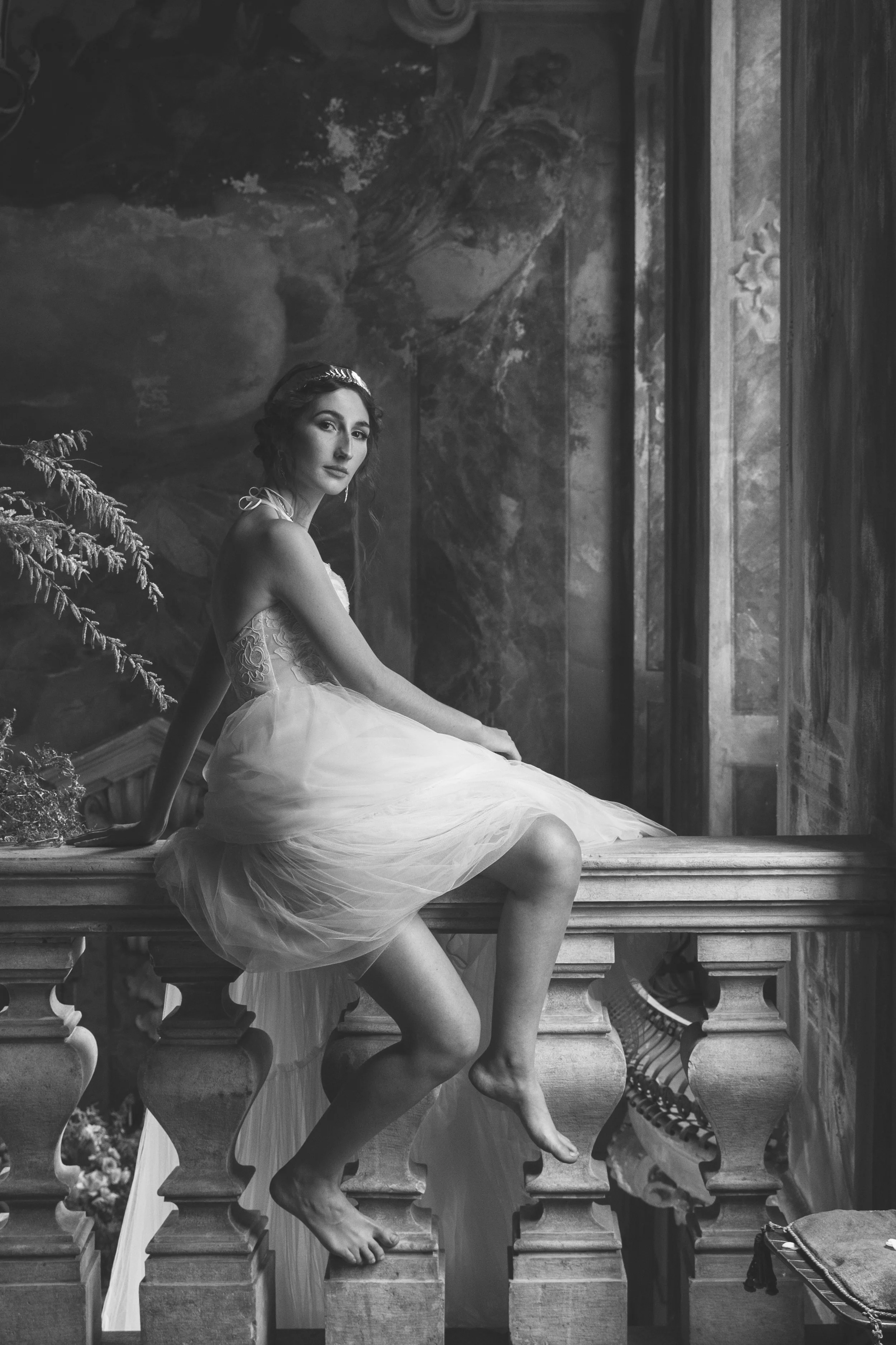 Donna in abito da sposa seduta su un balcone di marmo, in una stanza decorata con affreschi, in bianco e nero.