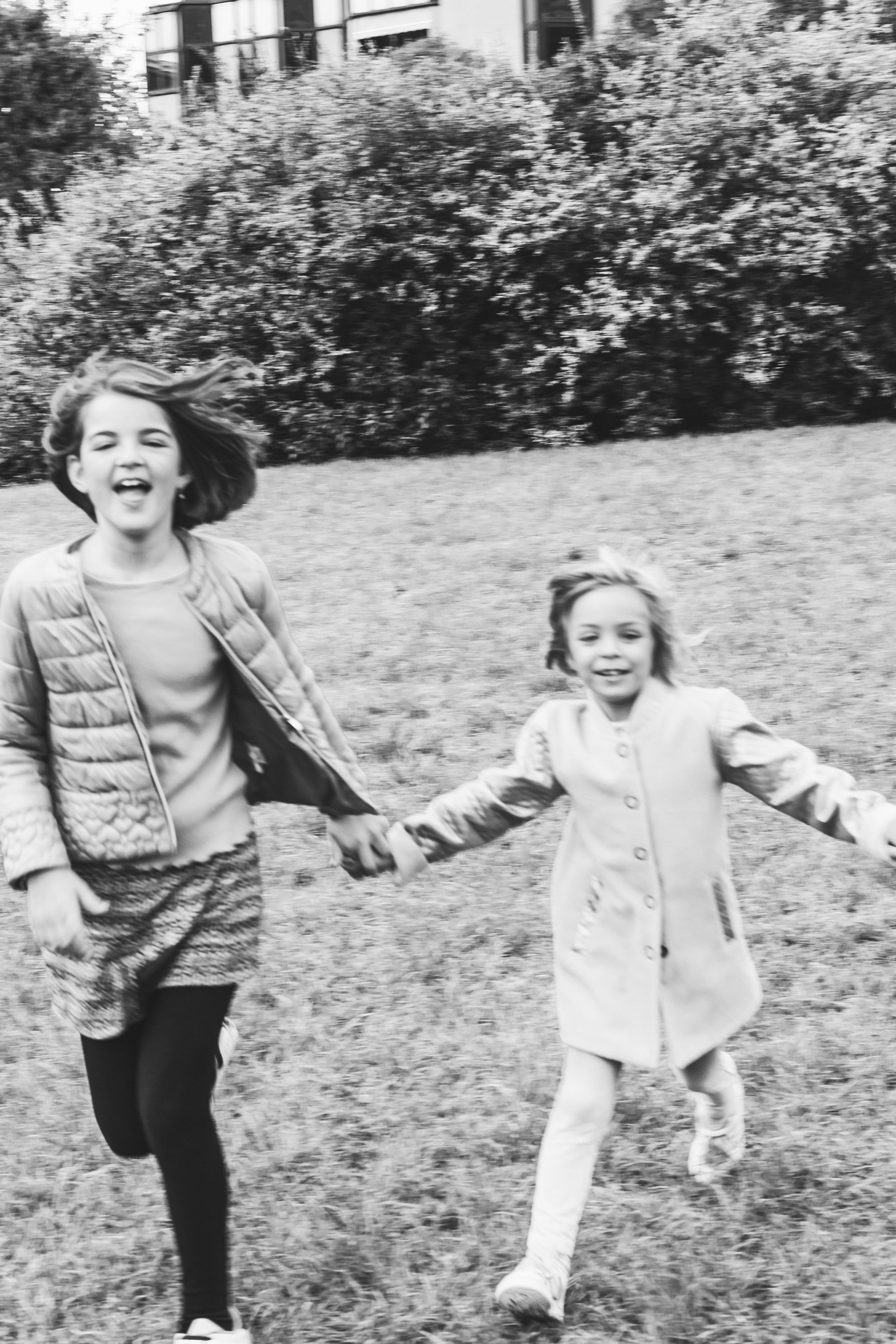 Due bambine che corrono e si tengono per mano in un parco, sorridendo.