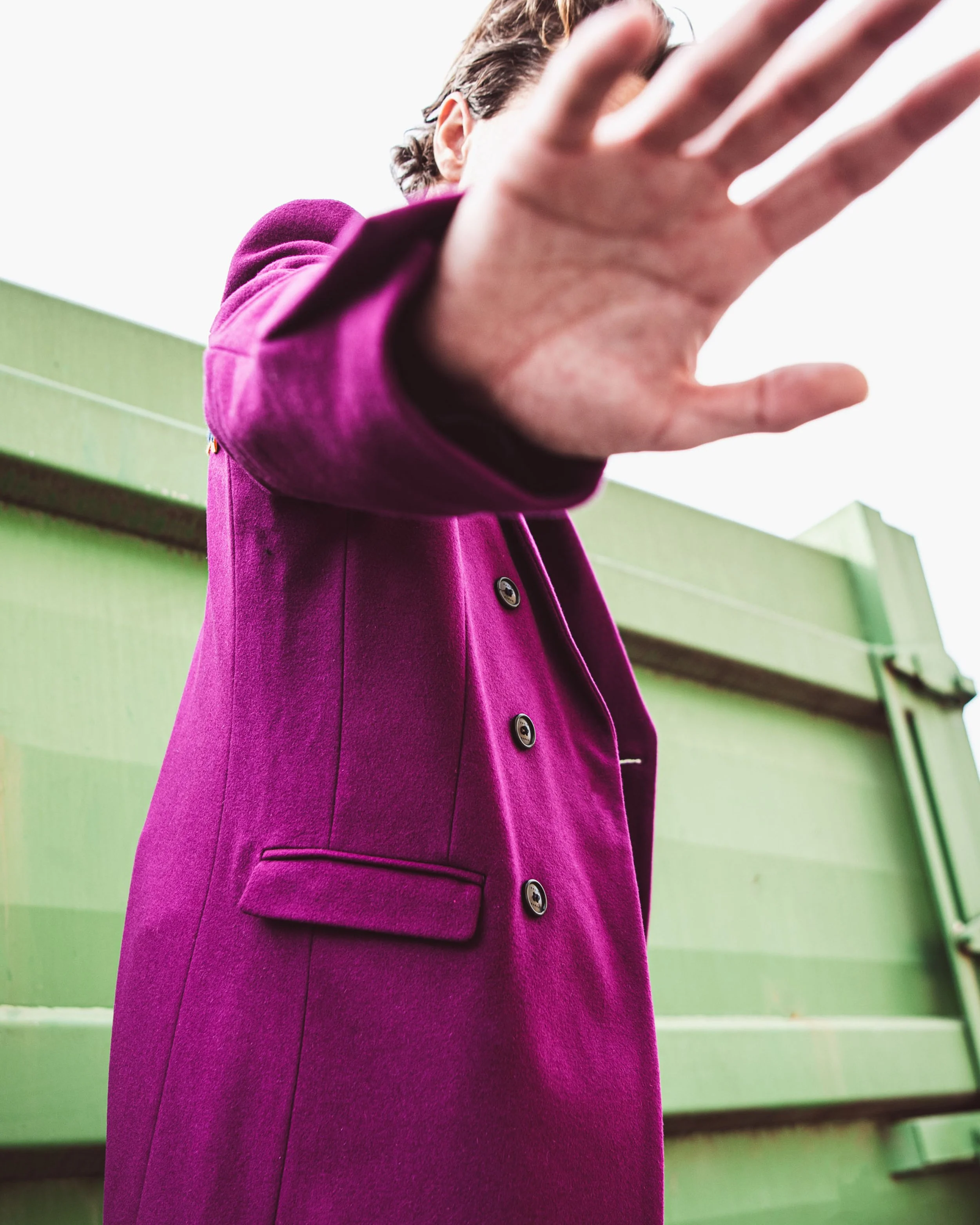 Persona che indossa un cappotto viola e si avvicina, con la mano tesa verso la fotocamera, spazio vuoto per il testo