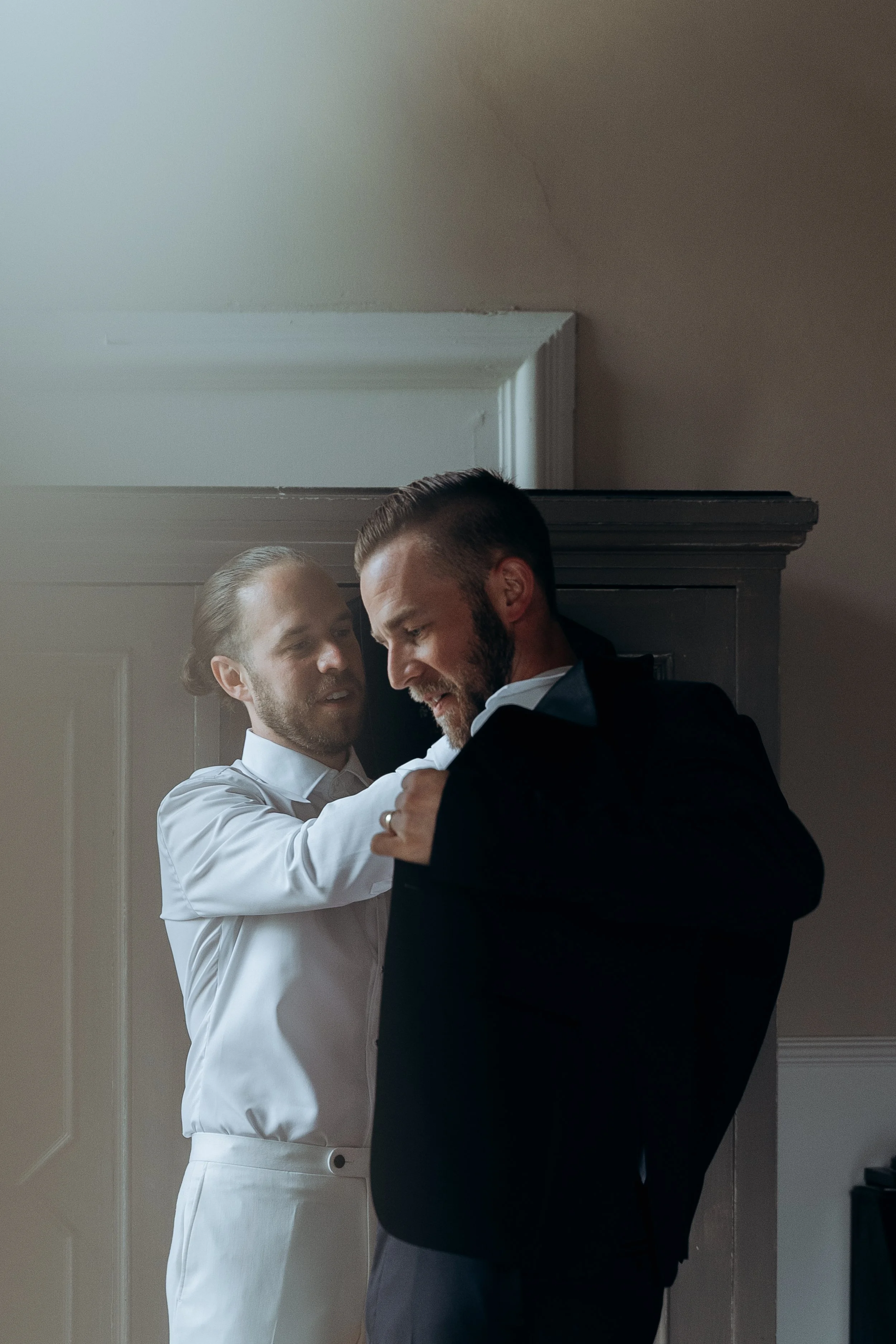 Due uomini vestiti elegantemente si aiutano a vestirsi in una stanza