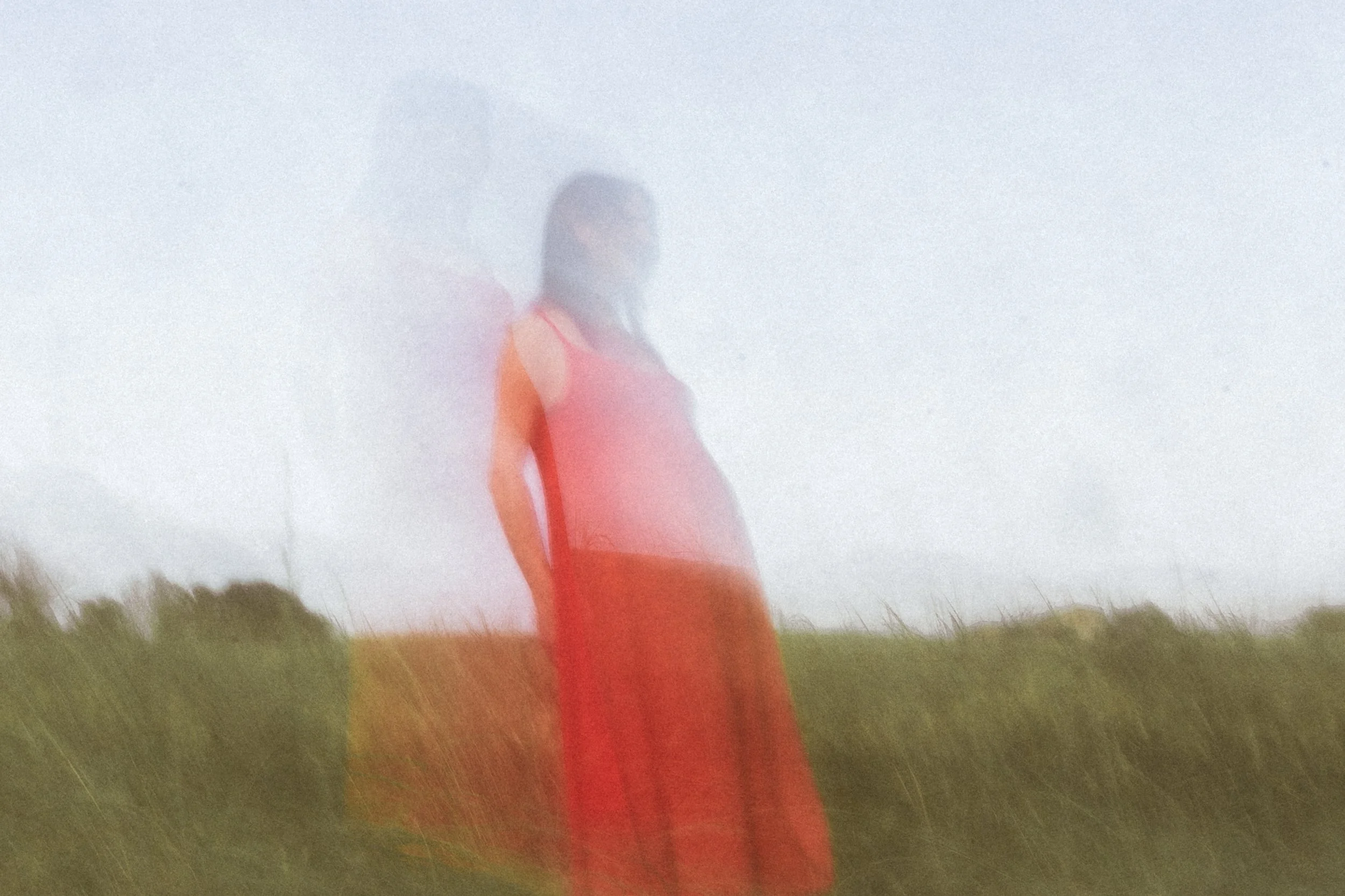 Figura di una donna incinta in un paesaggio aperto, vestita con un abito rosso, fotografata con un effetto di sfocatura e movimento.