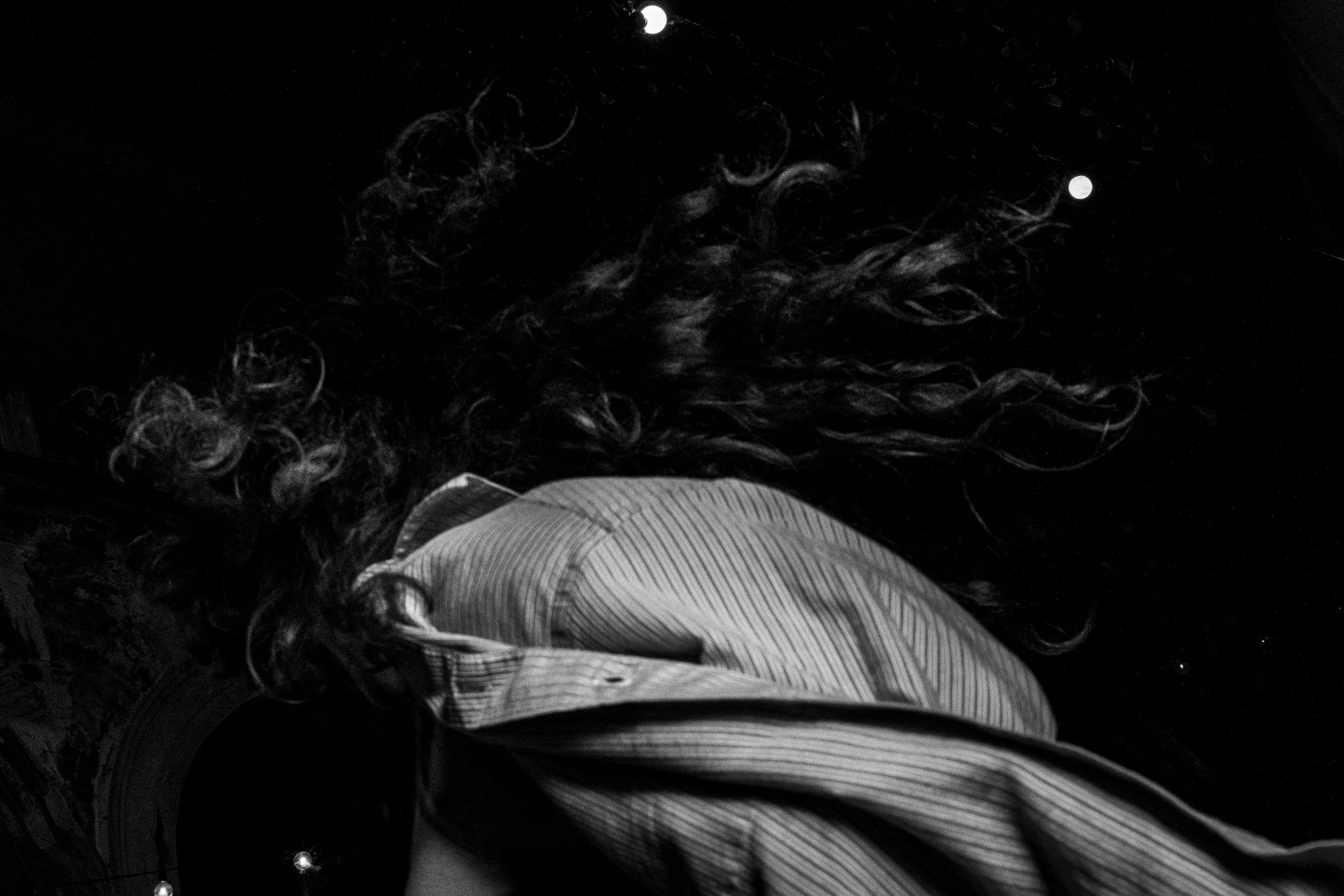 Velo con capelli lunghi e ricci, indossa una camicia a righe e si trova di notte con il cielo scuro e le stelle visibili.