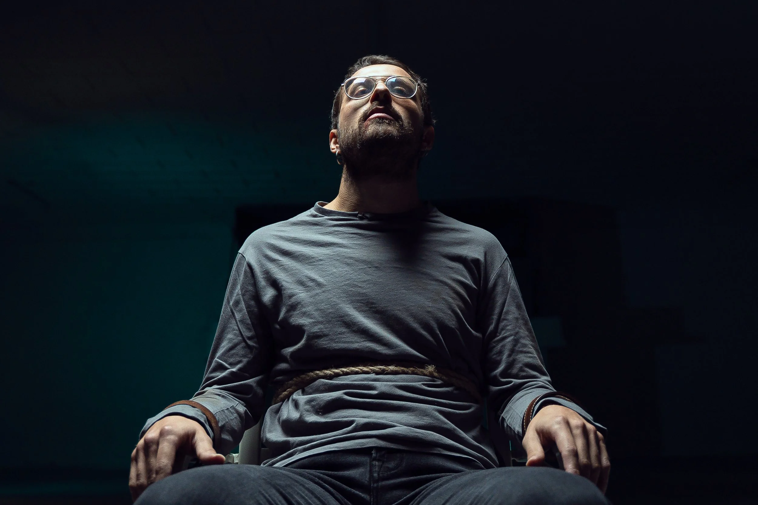 Un uomo seduto con le mani legate con una corda, in un ambiente oscuro