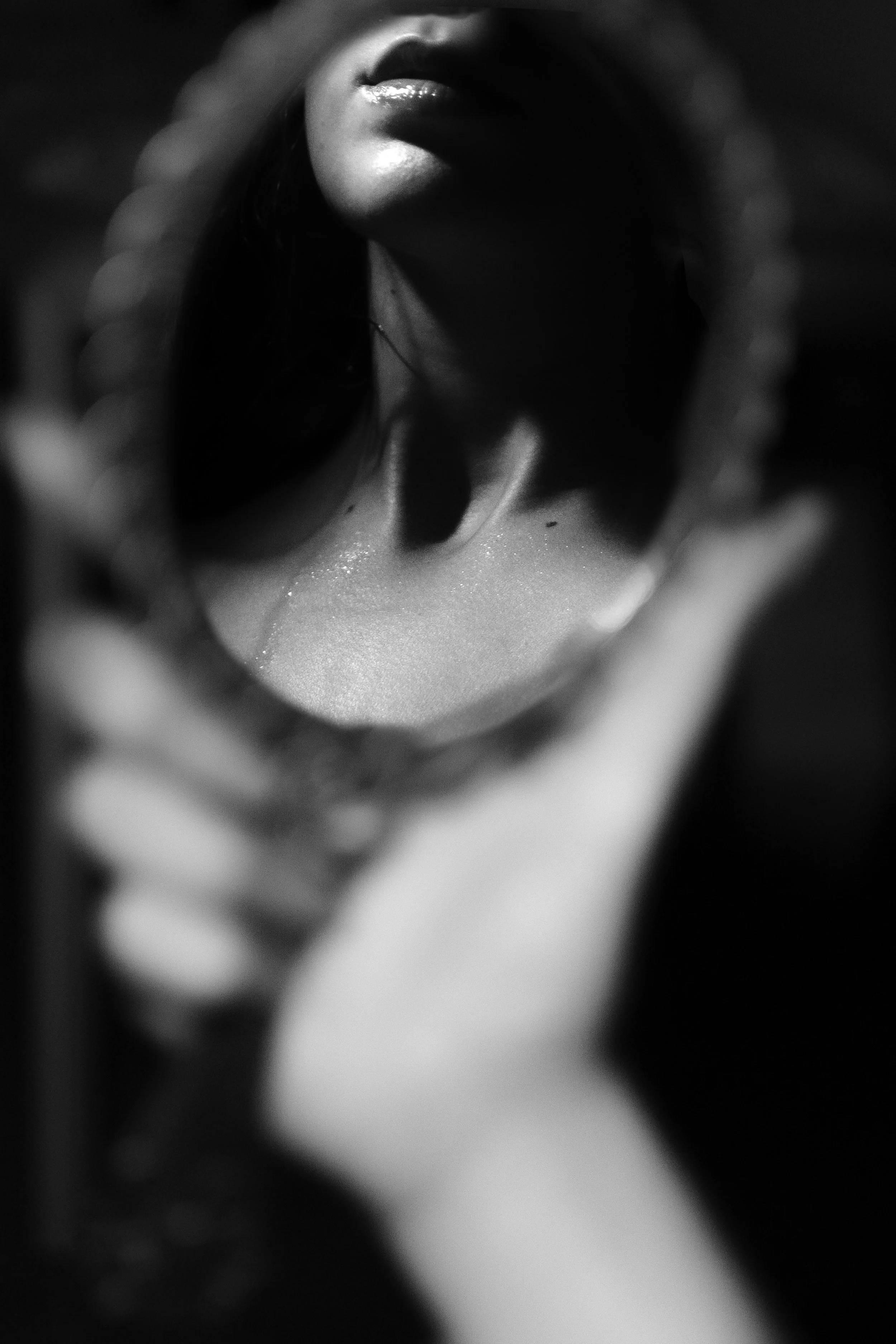 Ragazza che si guarda in uno specchio rotondo, viso in ombra e labbra lucide, in bianco e nero.