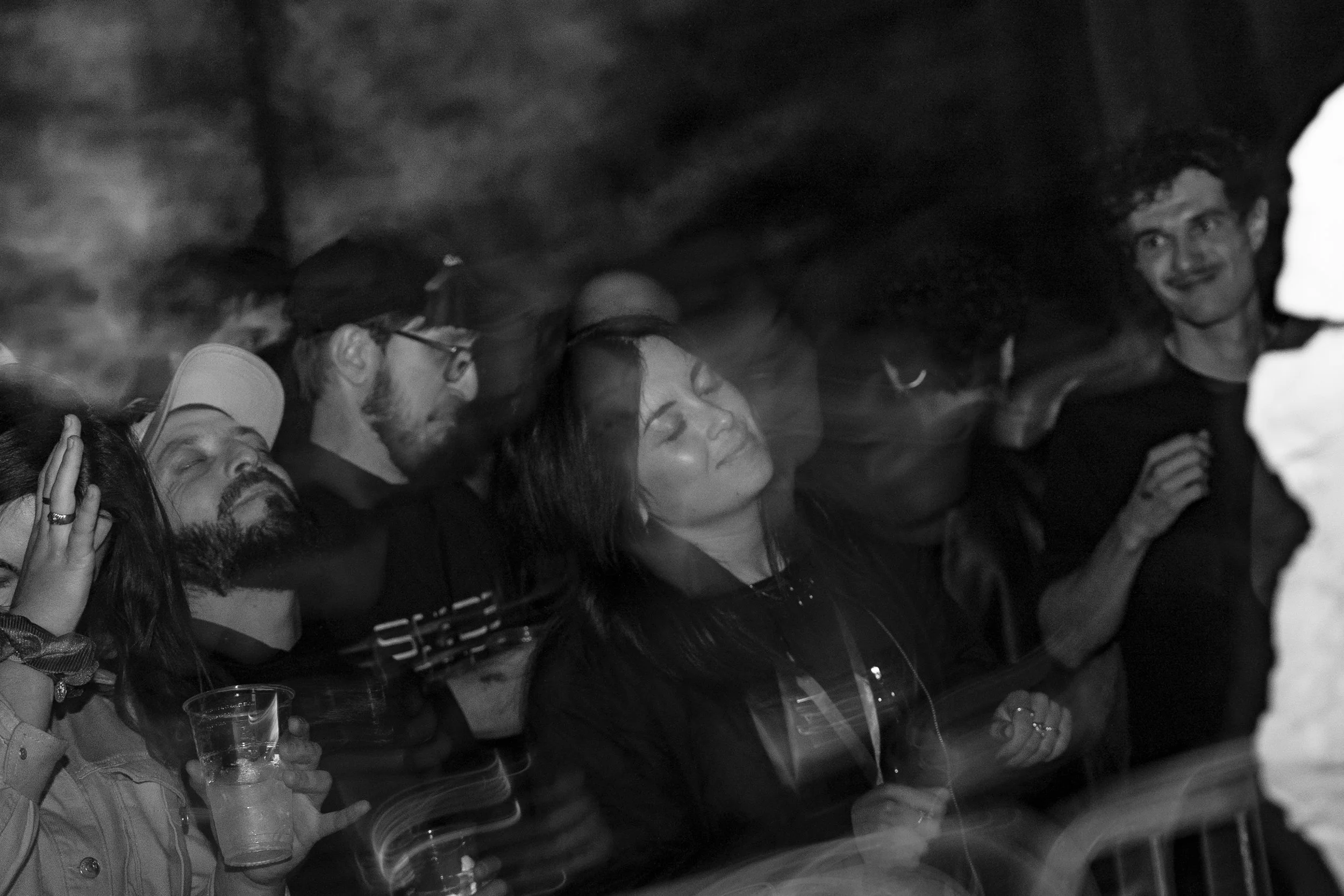 Un gruppo di persone che sembrano essere al concerto, alcune con gli occhi chiusi e che sembrano immerse nella musica, con luci e movimento attorno a loro.