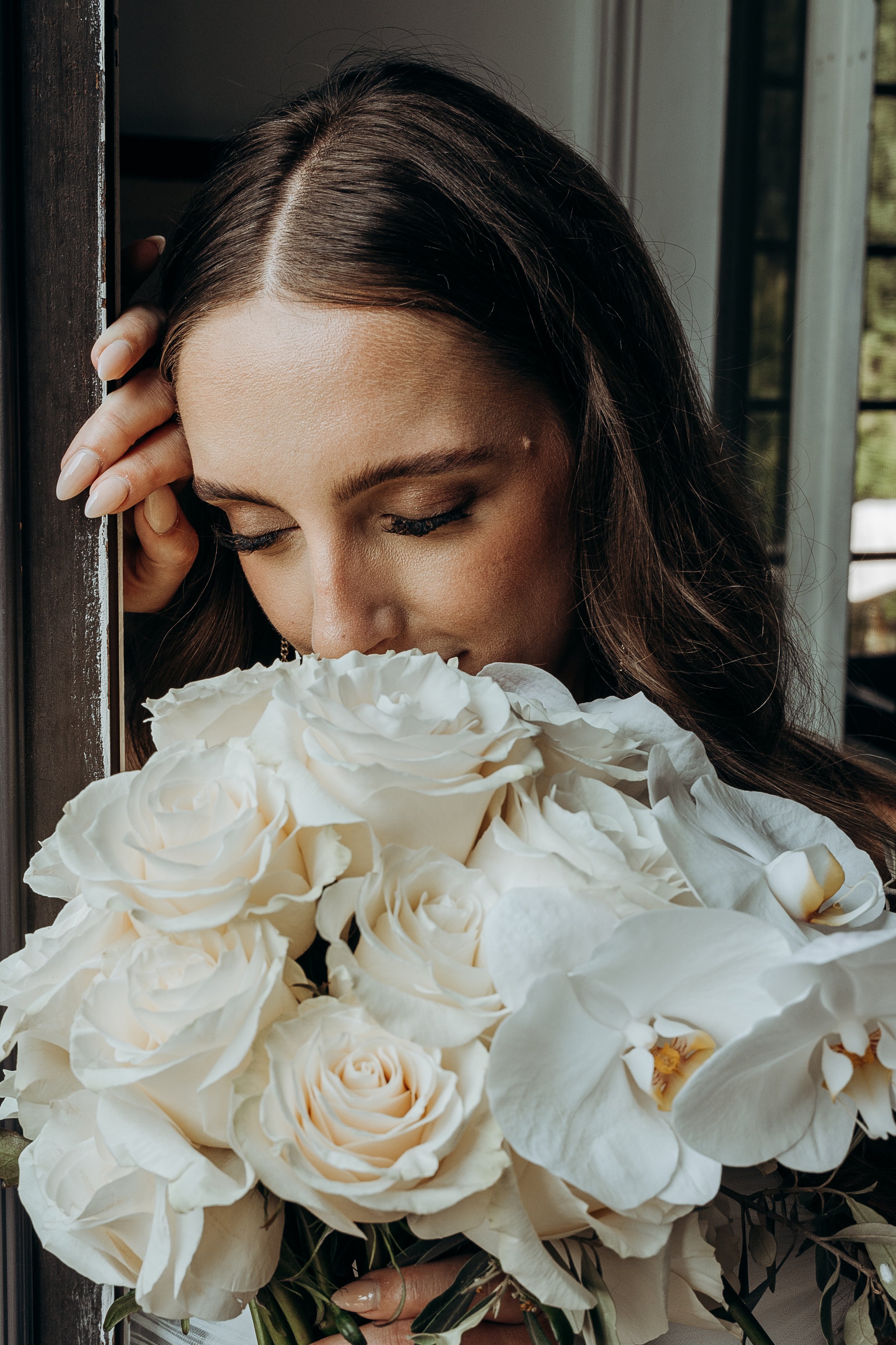 Una donna con i capelli castani occhi chiusi che profuma un grande bouquet di rose bianche.