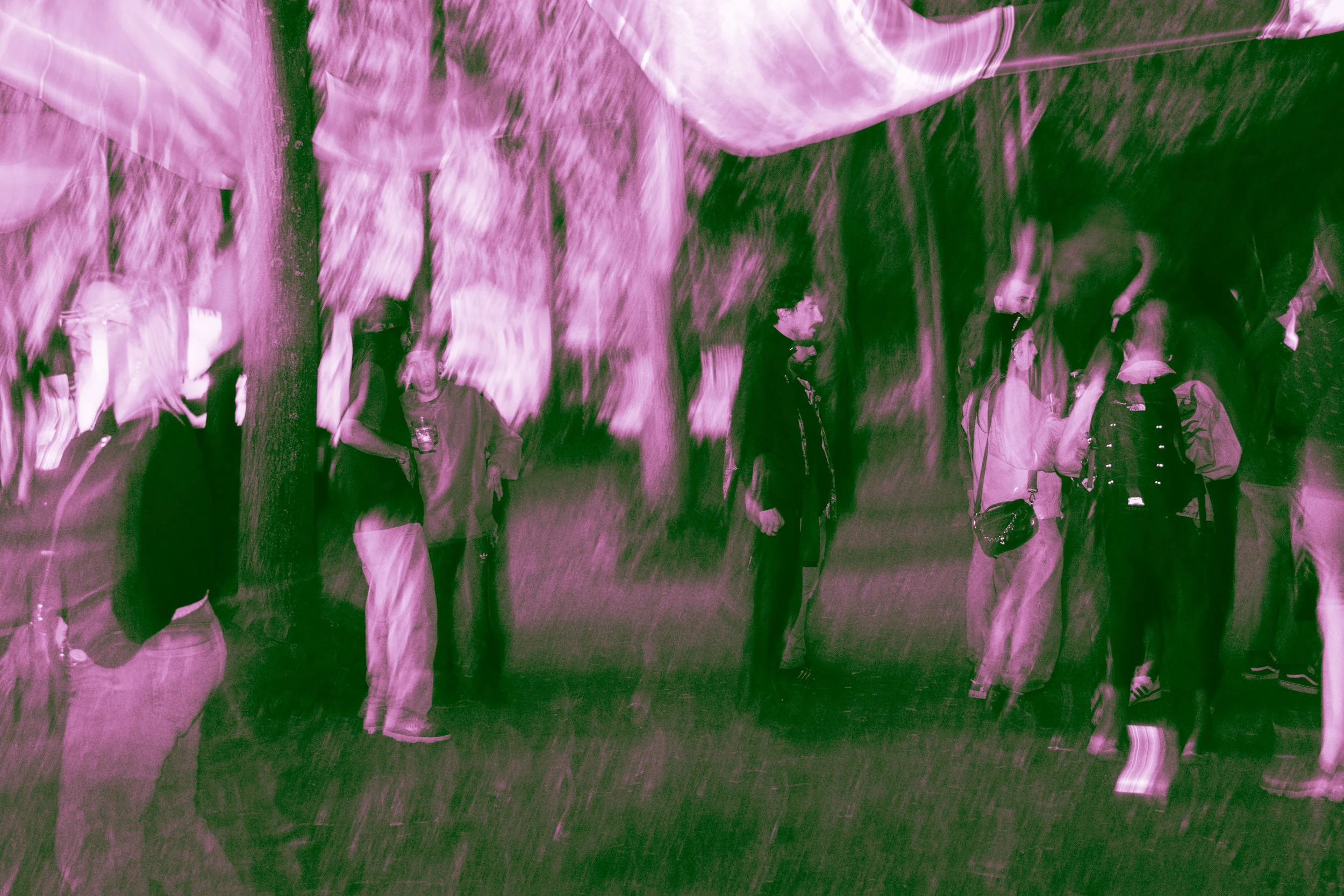 Gruppo di persone che si riuniscono sotto un riparo in un'area aperta con alberi, in un ambiente informale.