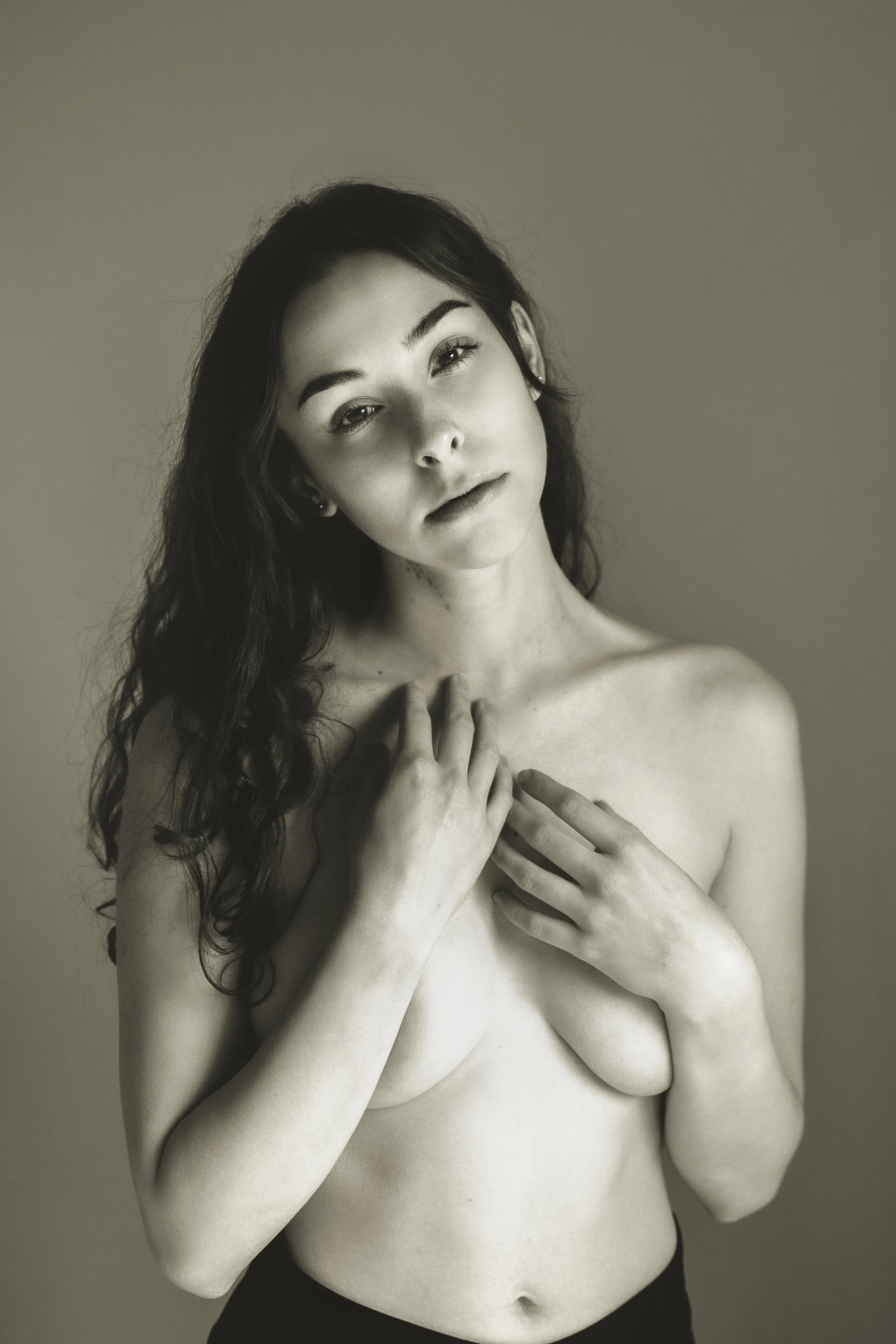 Ragazza nuda con capelli ricci, che si copre il torace con le mani, in una foto in bianco e nero.