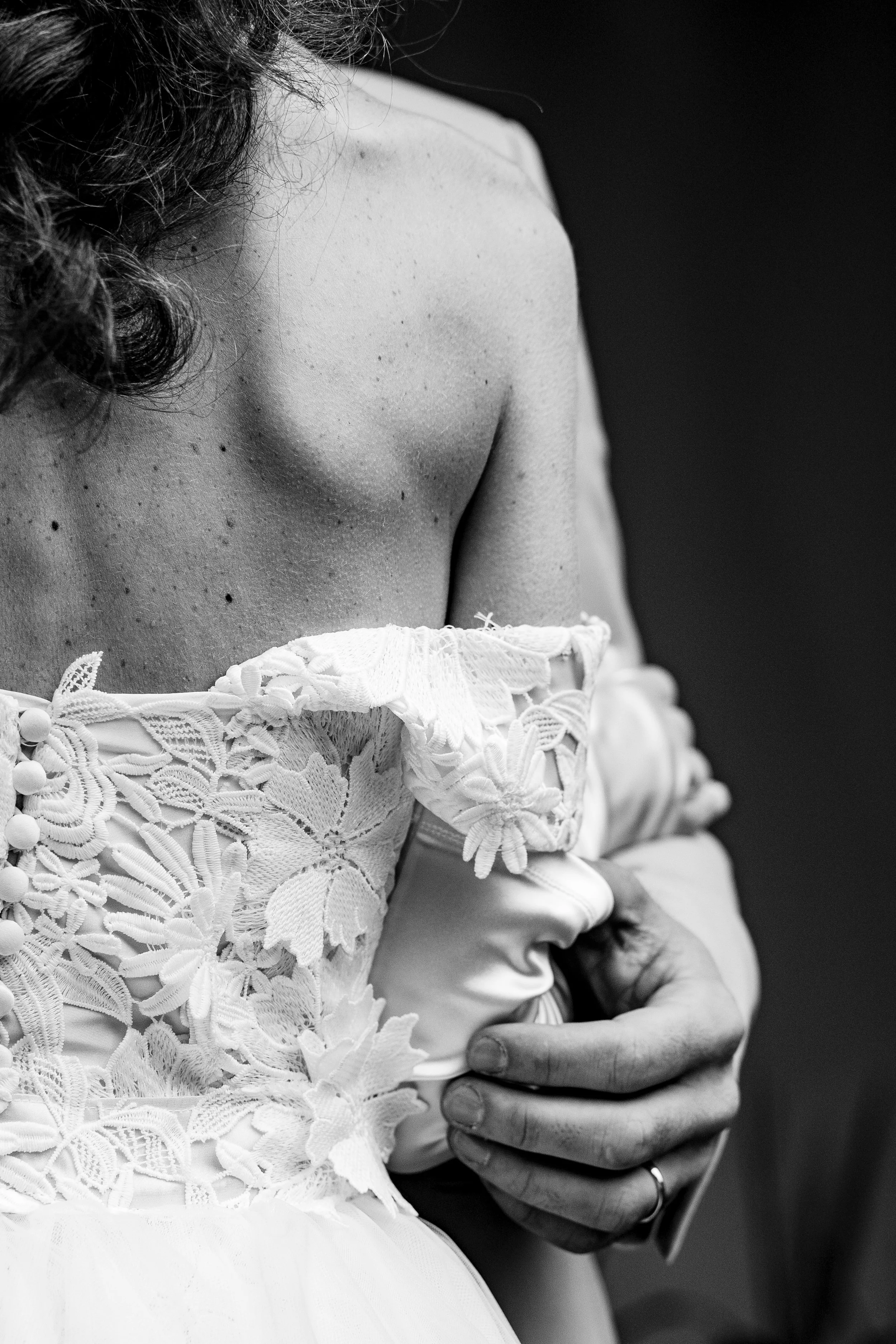 Una donna sta indossando un abito da sposa bianco con dettagli in pizzo e fiore, e si sta sistemando con le mani.