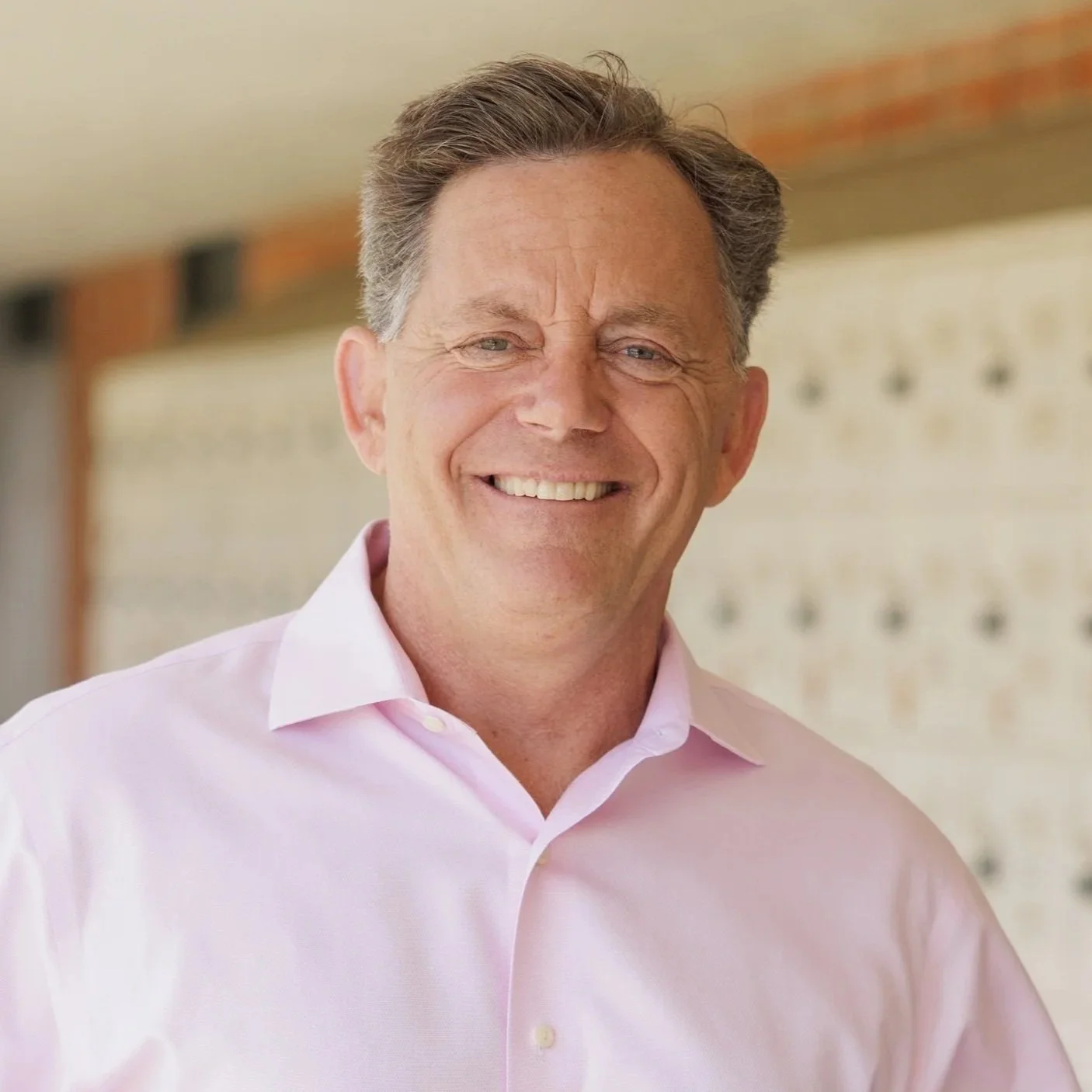 A middle-aged man with short brown hair, smiling and wearing a light pink dress shirt.