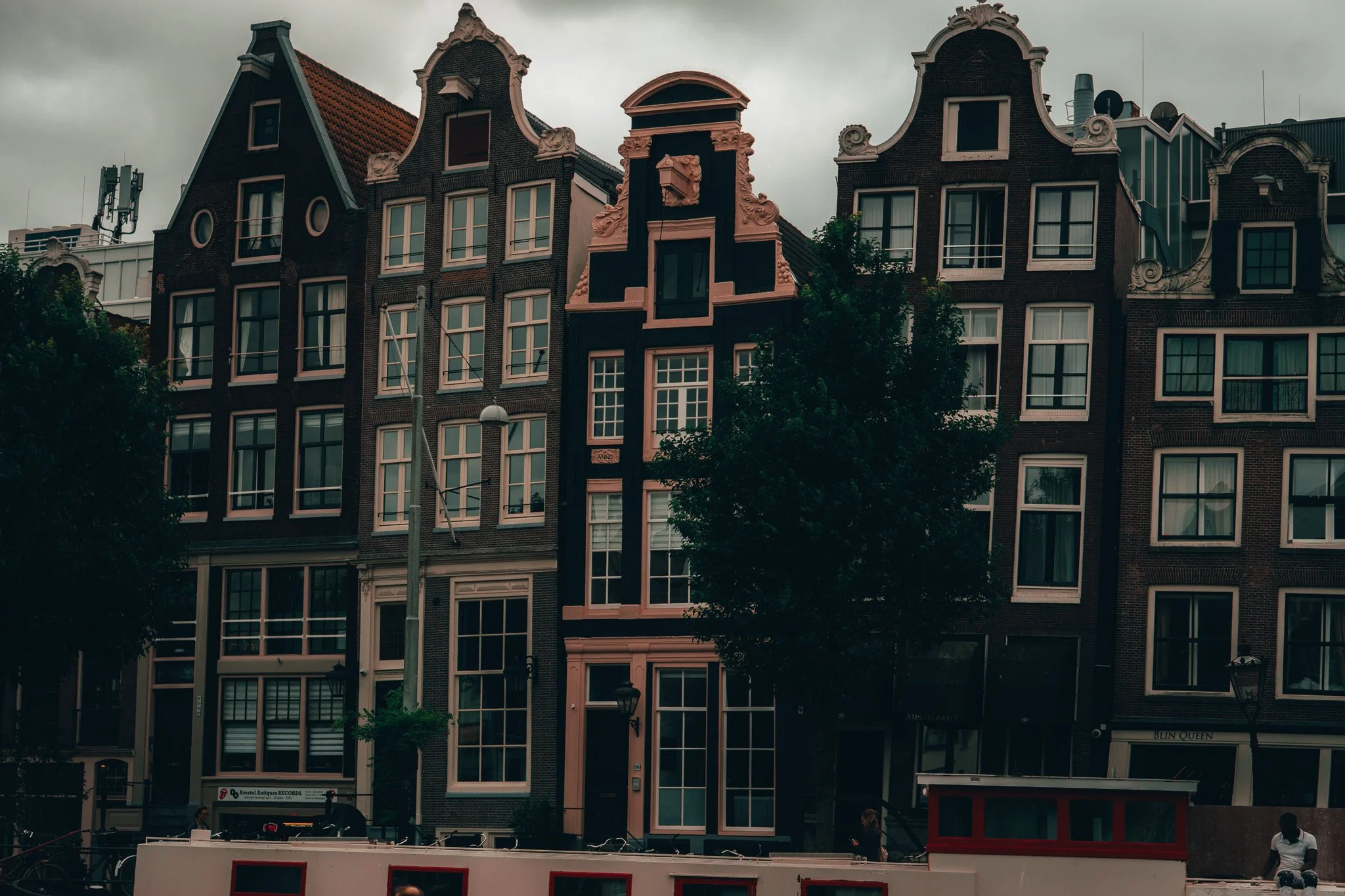 A row of traditional Dutch-style narrow, tall brick row houses with ornate gabled roofs along a street under a cloudy sky.
