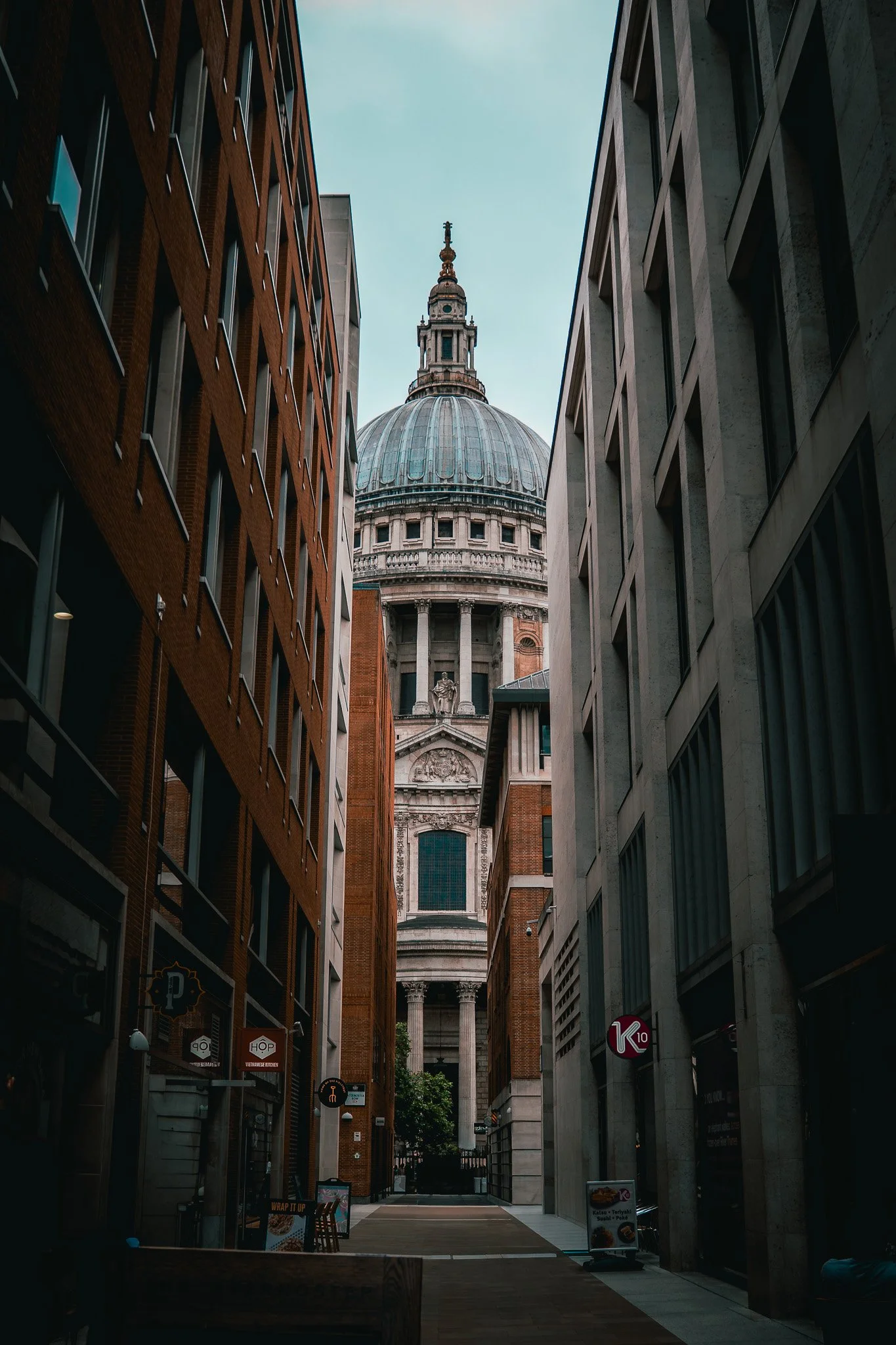 View of a narrow street with tall buildings on each side leading to an urban st. temple or historic building with a large dome in the background.