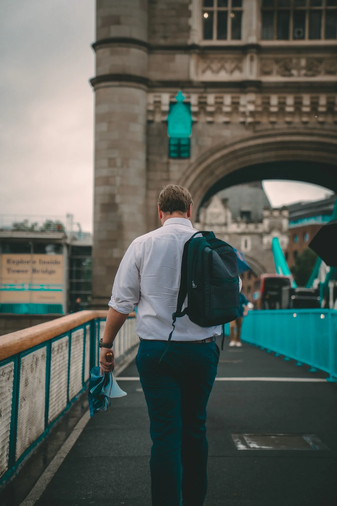 A man with a backpack walks under Tower Bridge in London, England.