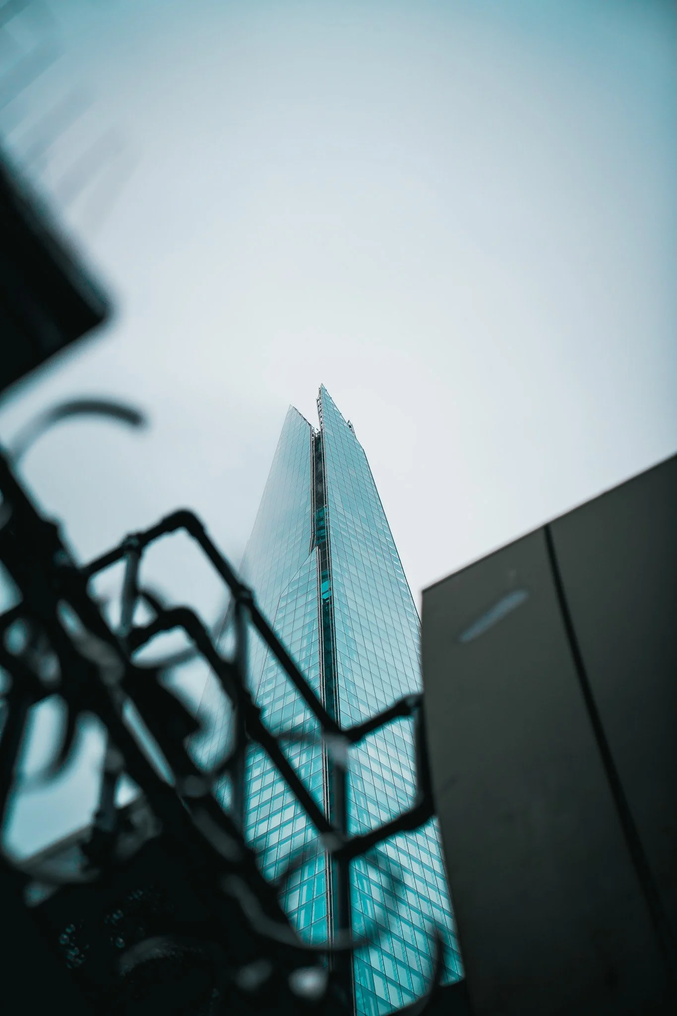 Low-angle view of a modern glass skyscraper against a pale sky, with part of a bicycle in the foreground.