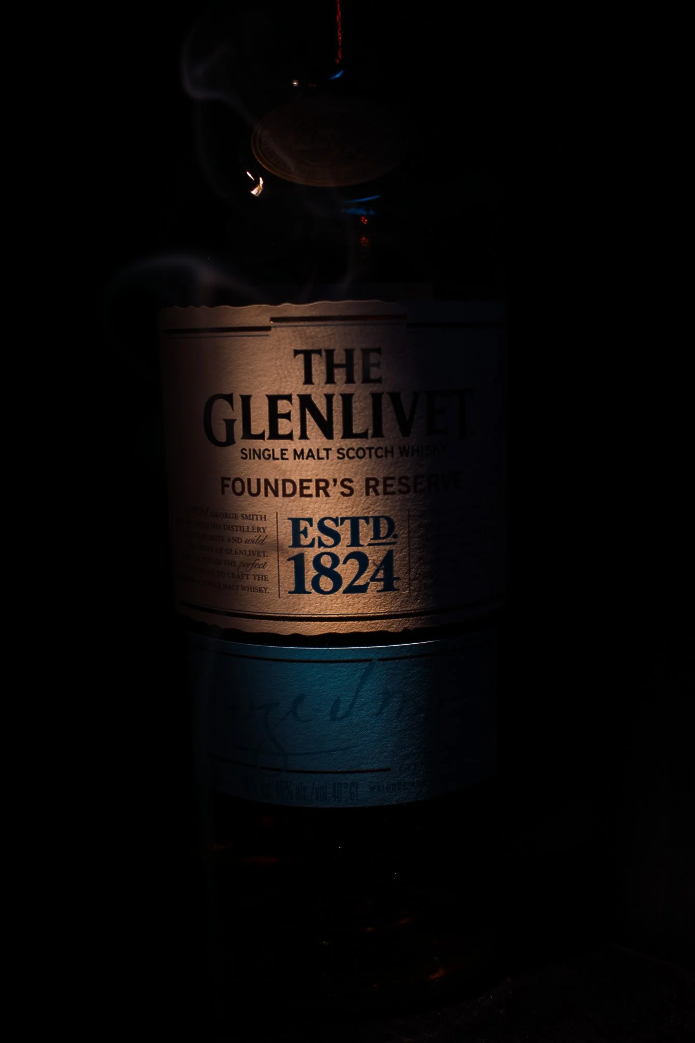 A bottle of The Glenlivet Founder's Reserve single malt Scotch whisky with a dark background and smoke or vapor around the bottle.