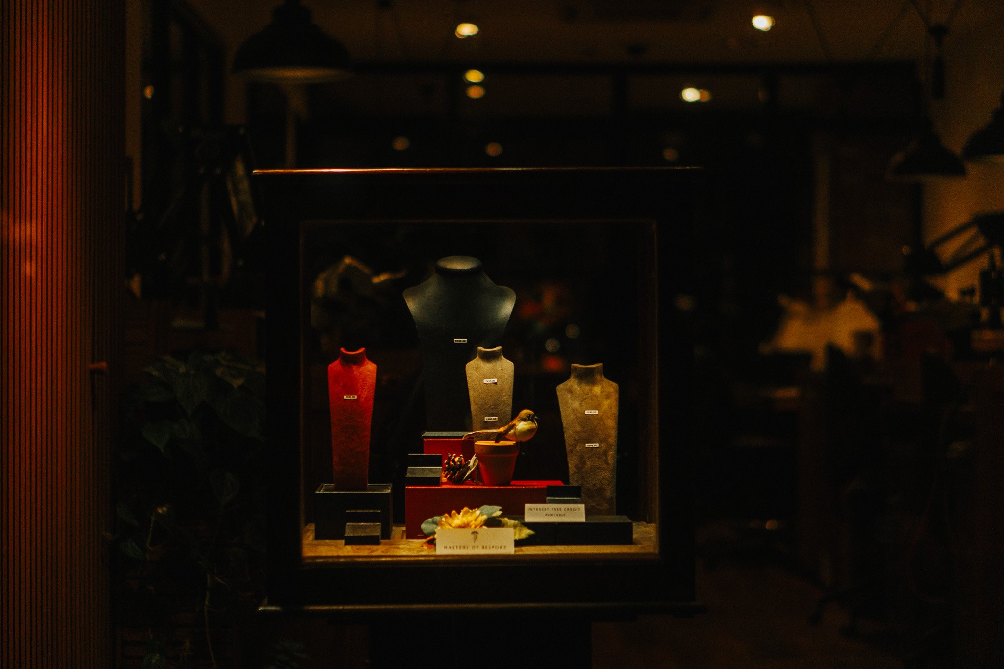 Display case with jewelry or accessories, featuring three mannequin busts in black, red, and beige, and decorative items inside a dimly lit store or showroom.