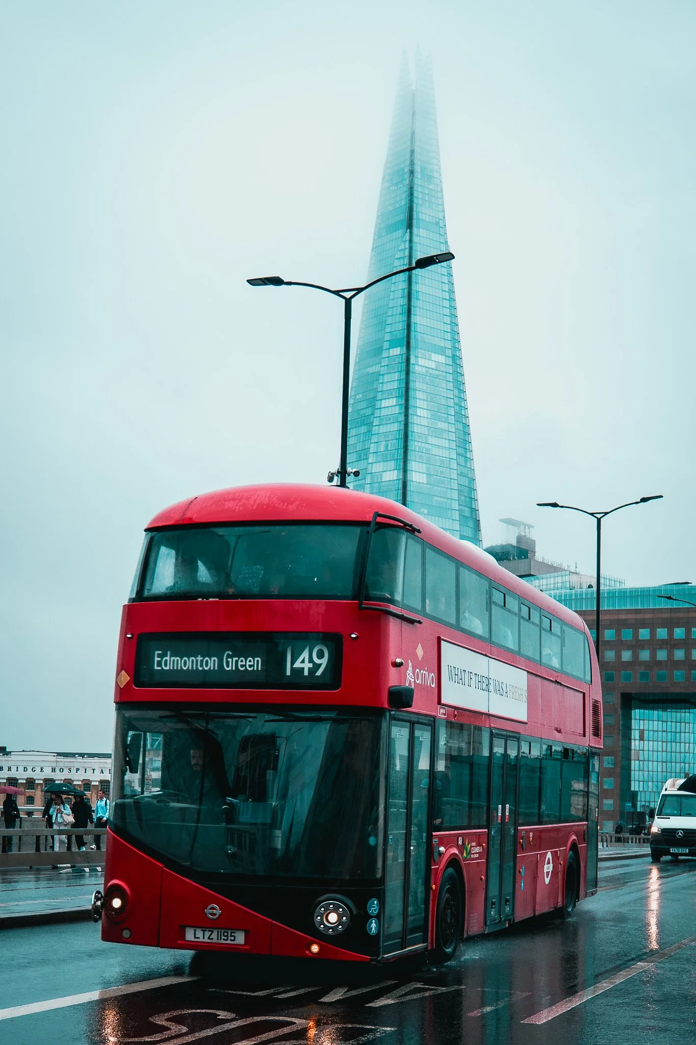 A red double-decker bus on a wet street in London with The Shard skyscraper in the background.