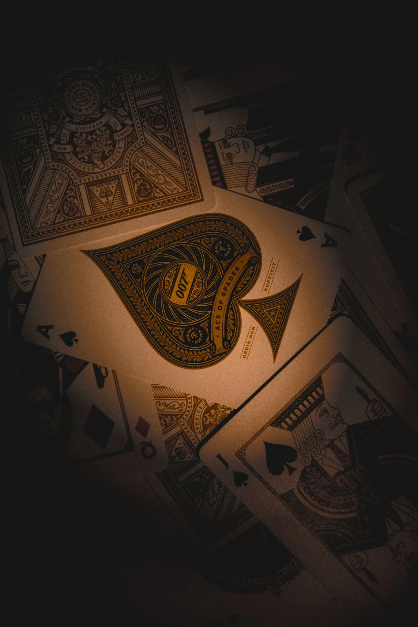 A deck of playing cards with a hidden background, showing the Ace of Spades prominently in the foreground, among other face cards and cards lying on a dark surface.